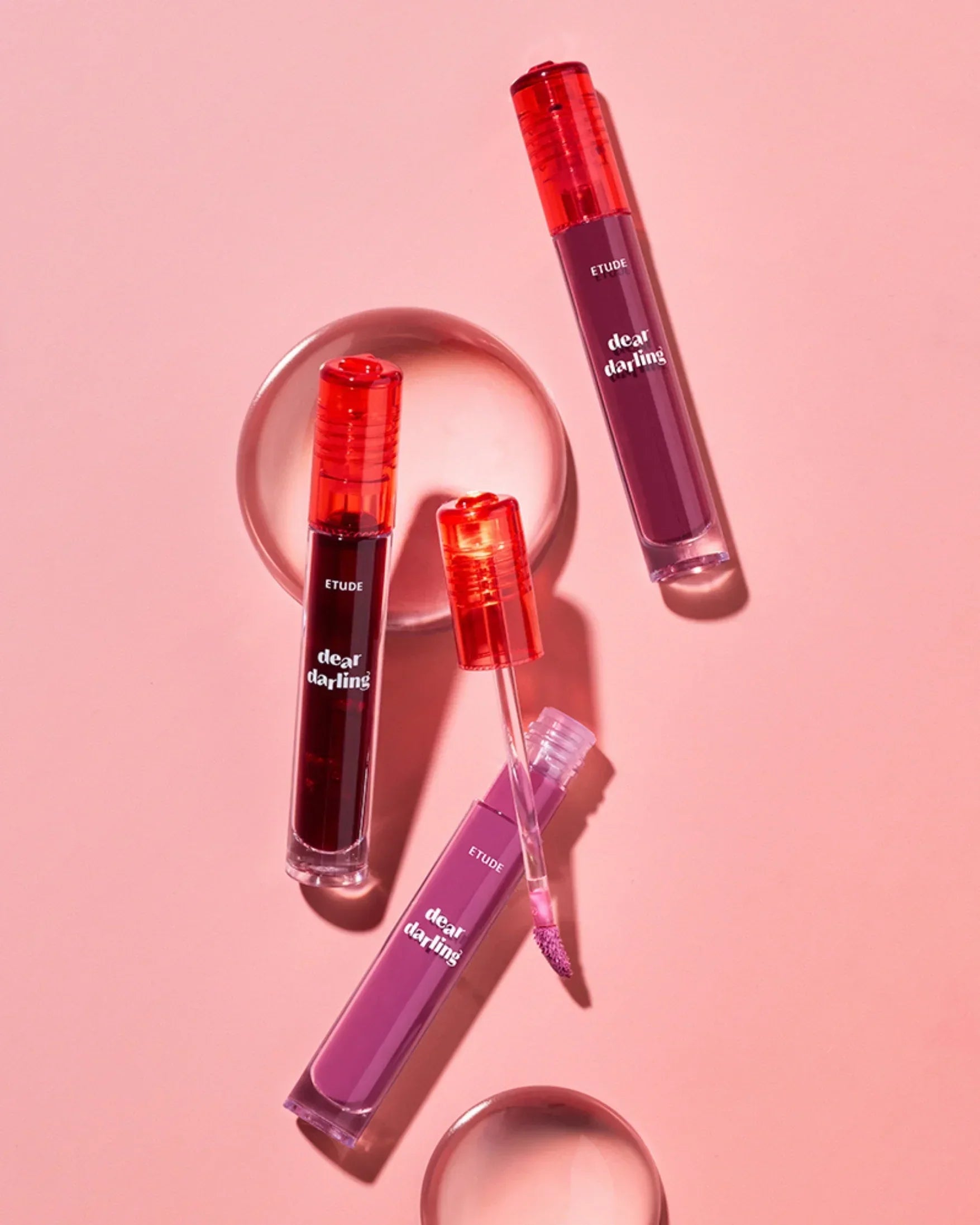 Etude Dear Darling liquid lipsticks in red and mauve with applicator on pink background
