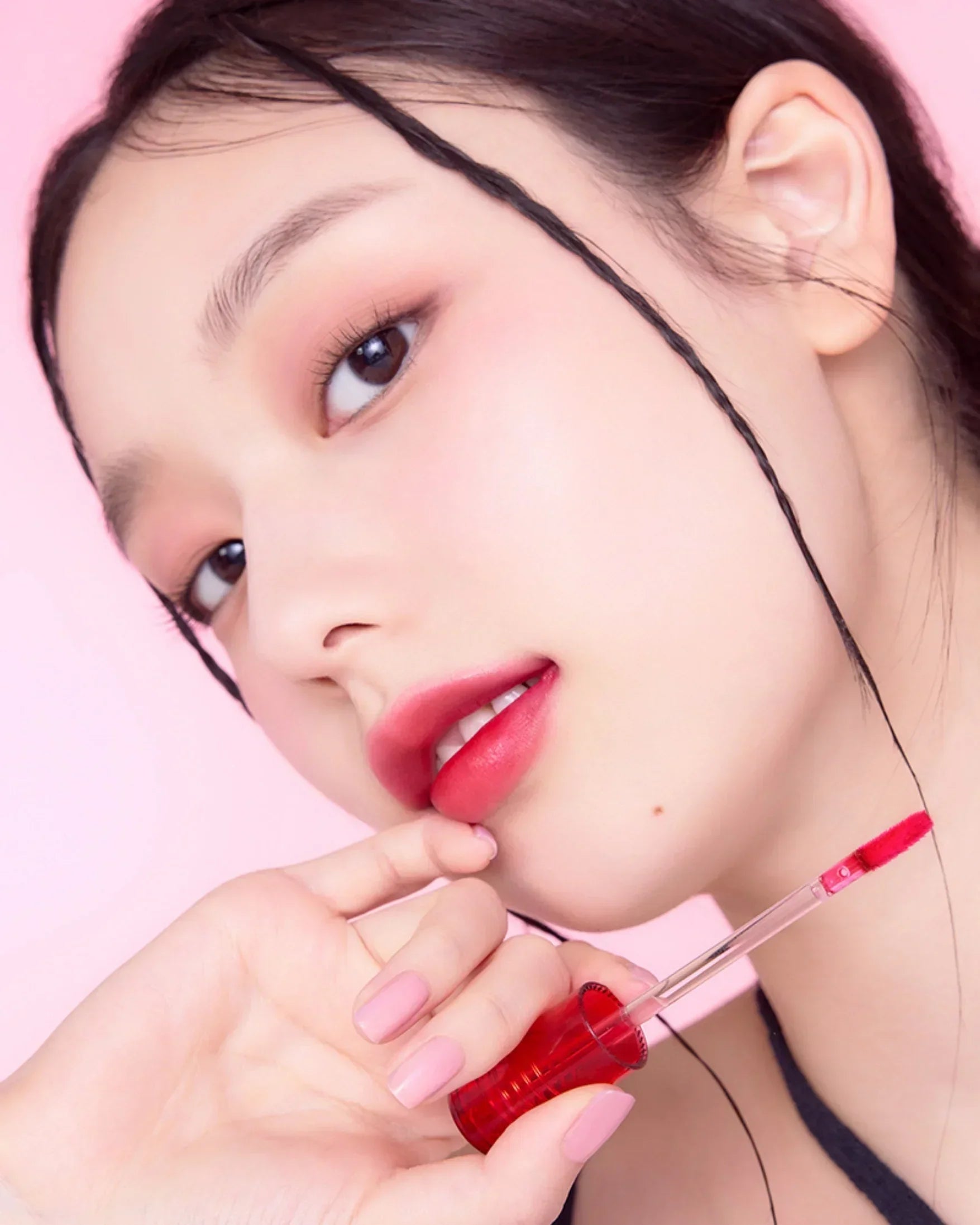 Close-up of woman with red lip tint and soft pink nails on pink background, highlighting glossy lip makeup