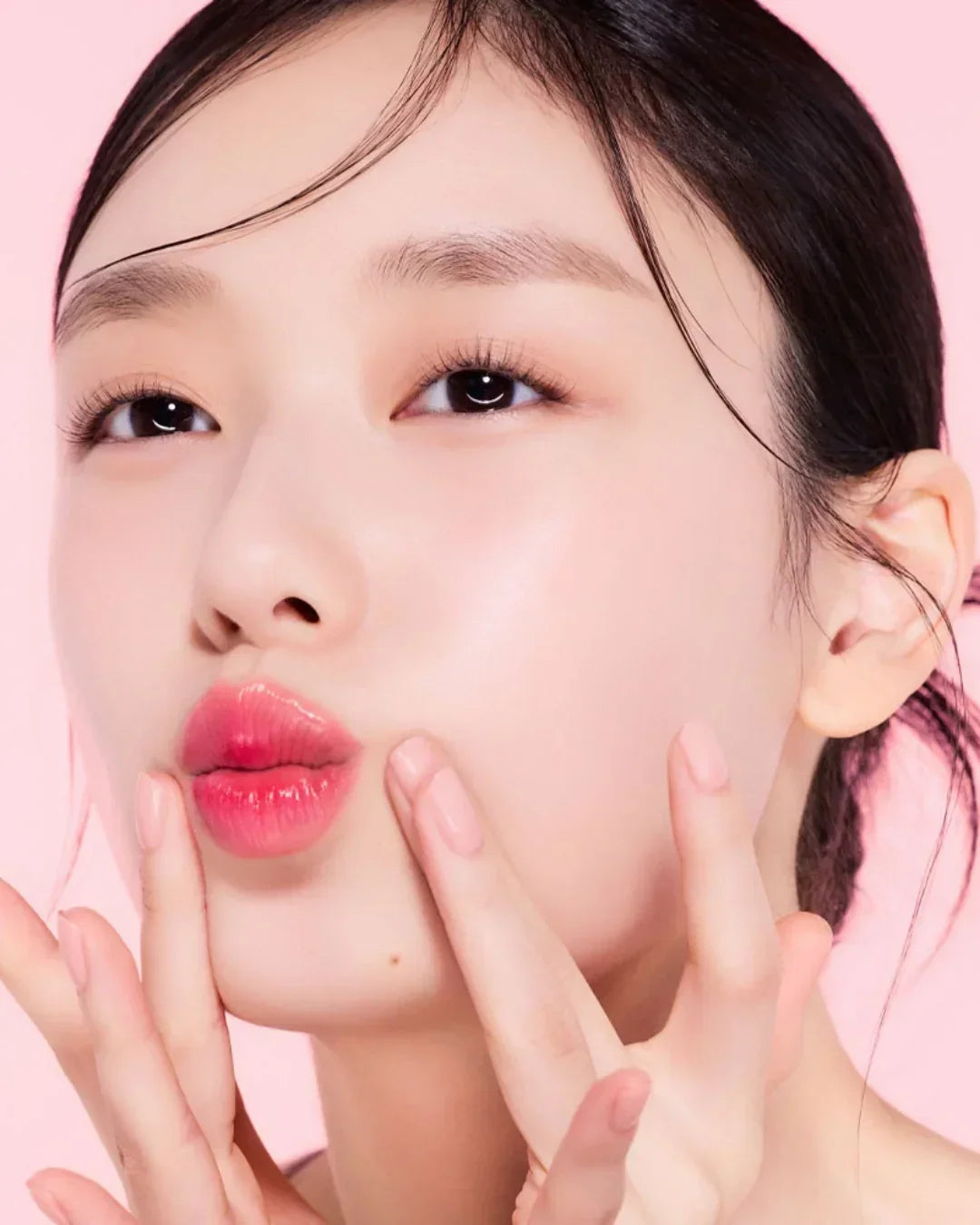 Close-up of woman with glossy pink lips, clear skin, and natural makeup on pink background