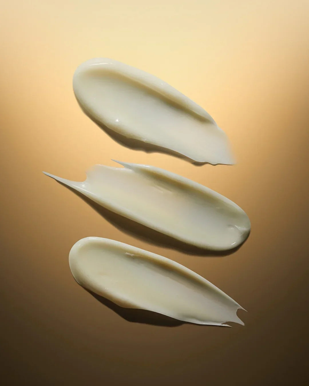 Three smooth, creamy white cosmetic cream swatches on warm beige background, showing texture and consistency
