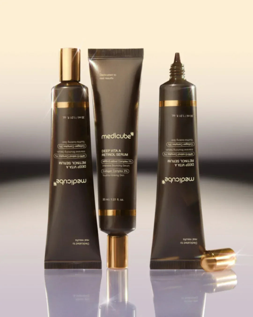 Three black and gold tubes of Medicube Deep Vita A Retinol Serum on reflective surface with soft gradient background