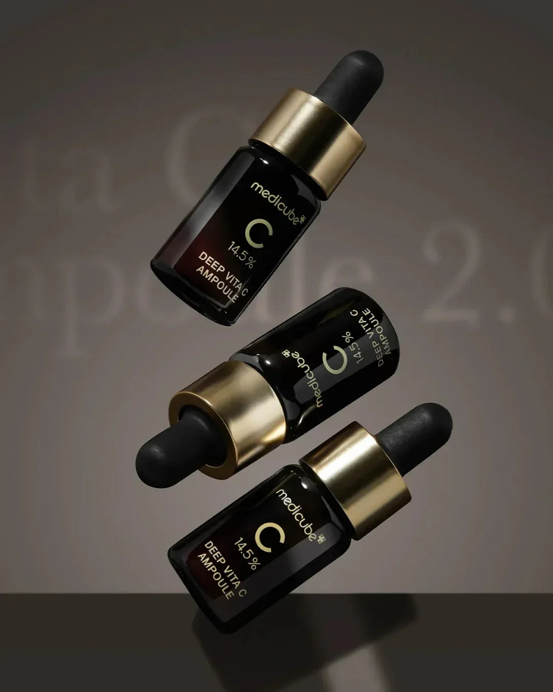 Three Medicube Deep Vita C Ampoule 14.5% bottles with gold caps and black droppers on dark background