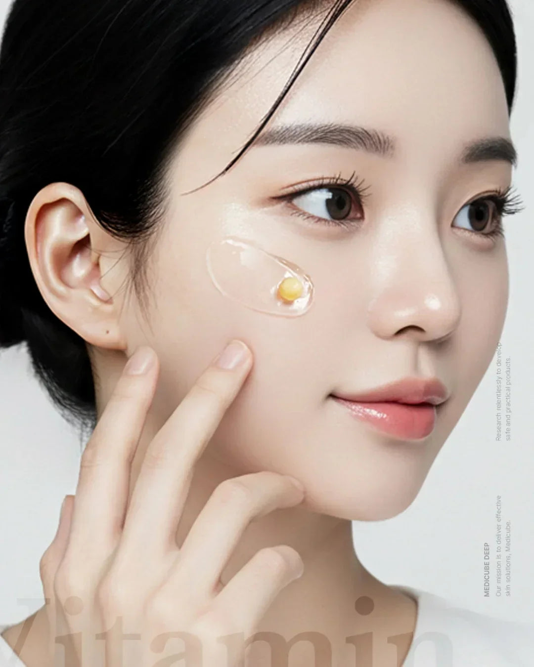 Close-up of woman applying clear cream with yellow vitamin C capsule on cheek for skincare