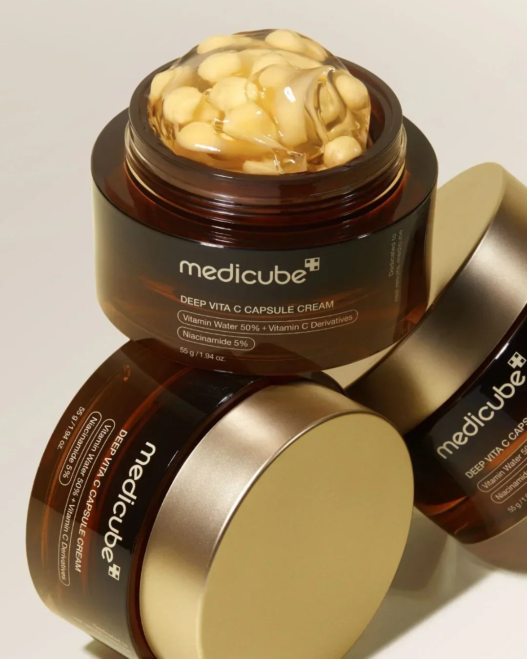 Open jar of Medicube Deep Vita C Capsule Cream with golden capsules, two closed jars on beige background