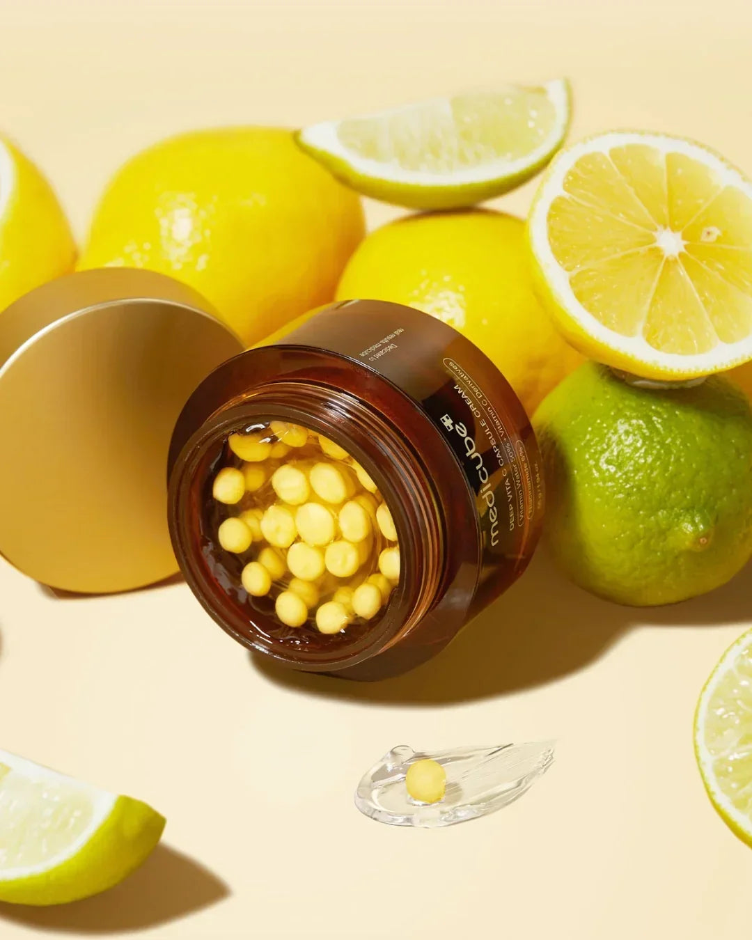 Open jar of Mediceuticals Deep Vita C capsules cream surrounded by fresh lemons and limes on beige background