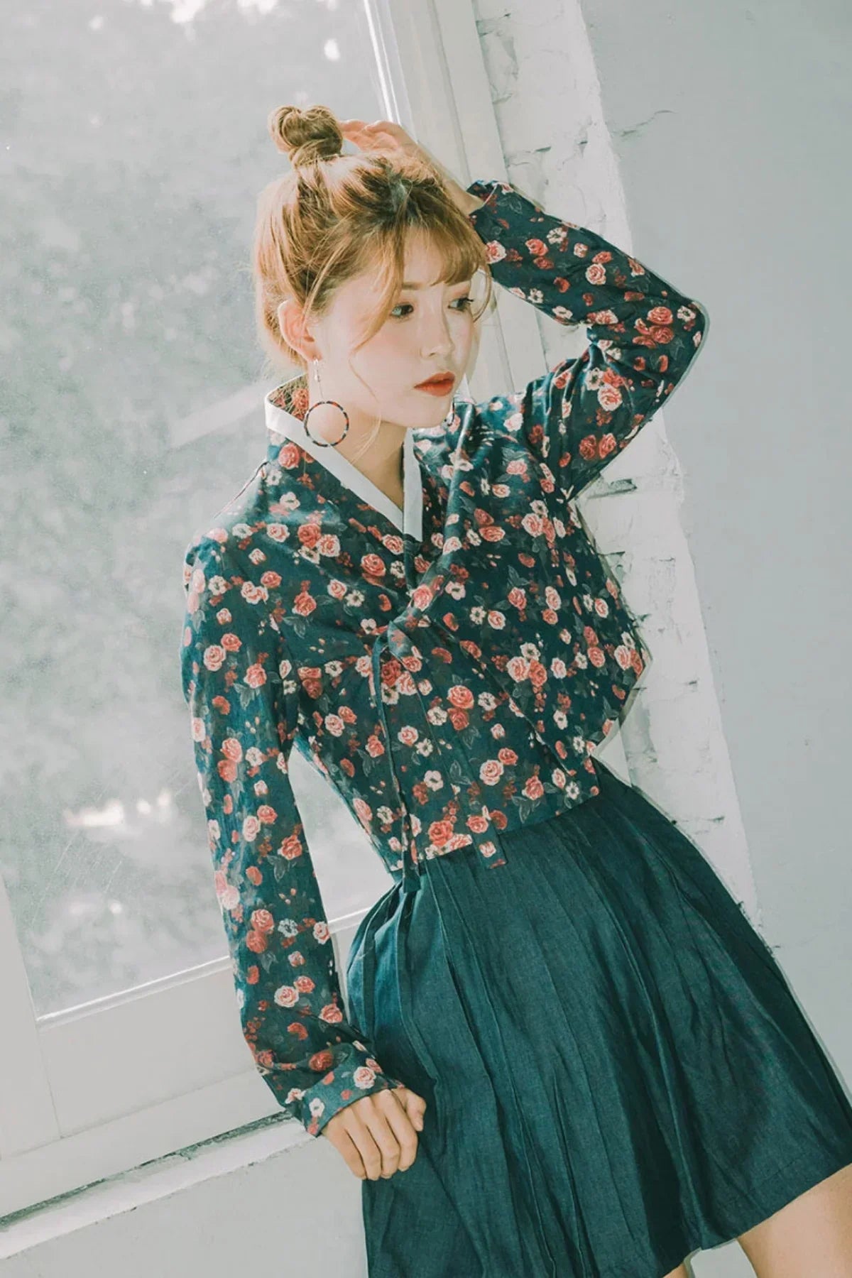 Young woman wearing vintage floral crop jacket and pleated dark blue skirt by window