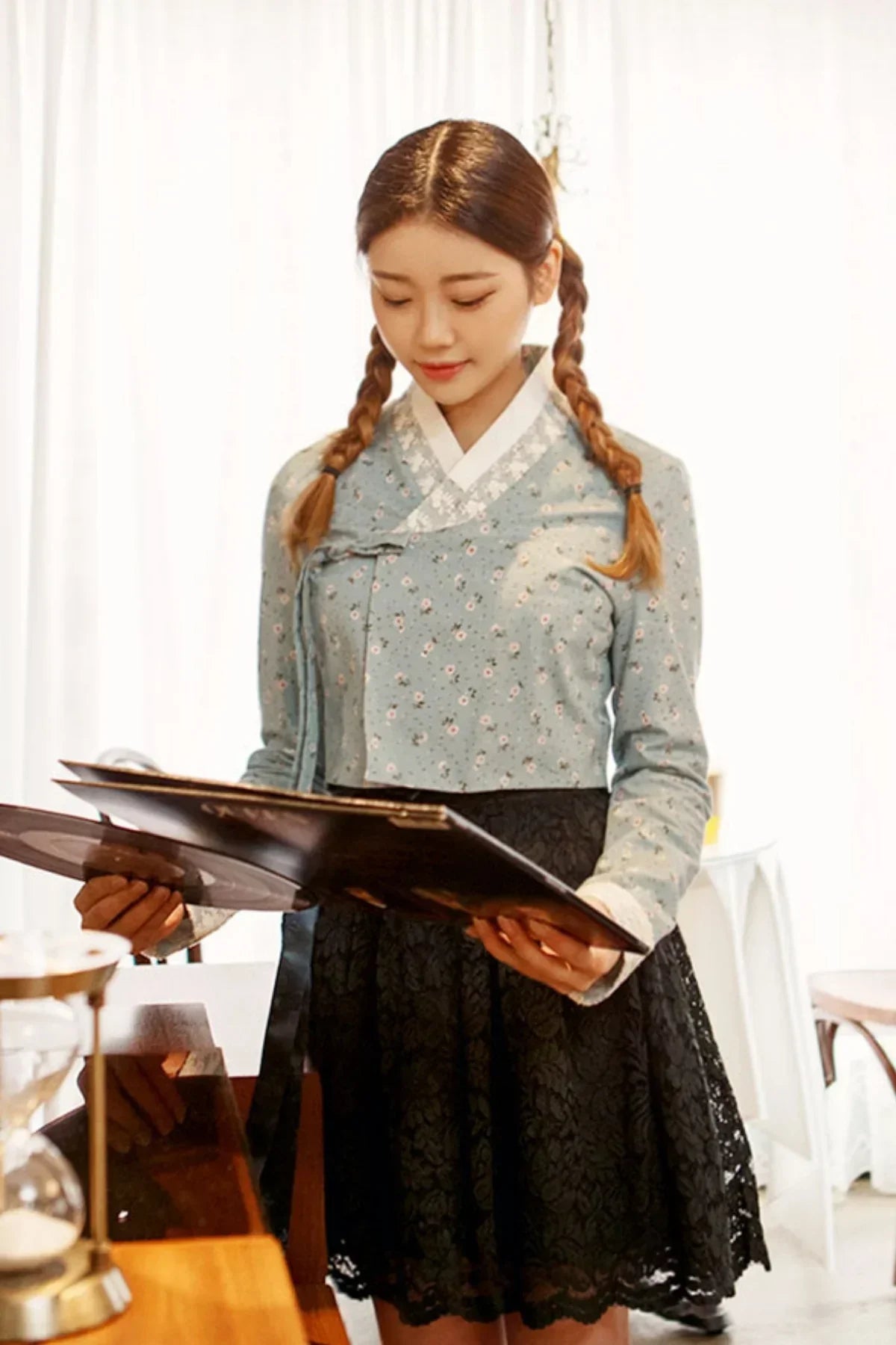 Young woman in traditional Korean hanbok top and black lace mini skirt reading a book indoors