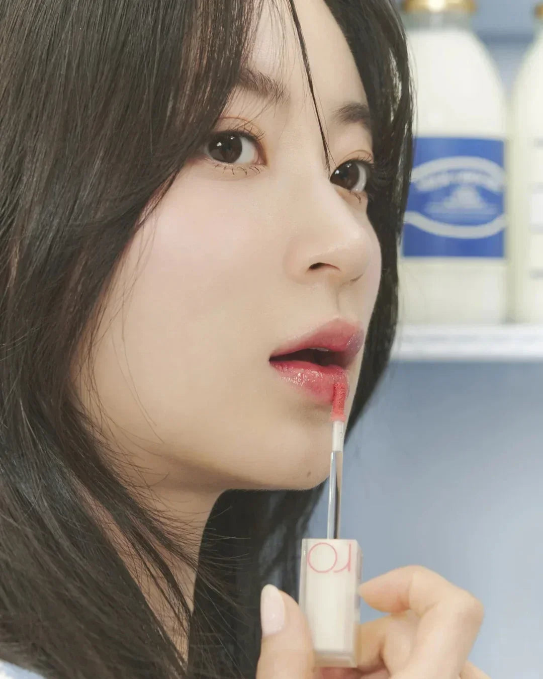 Close-up of woman applying pink lip tint with applicator, smooth skin and dark hair