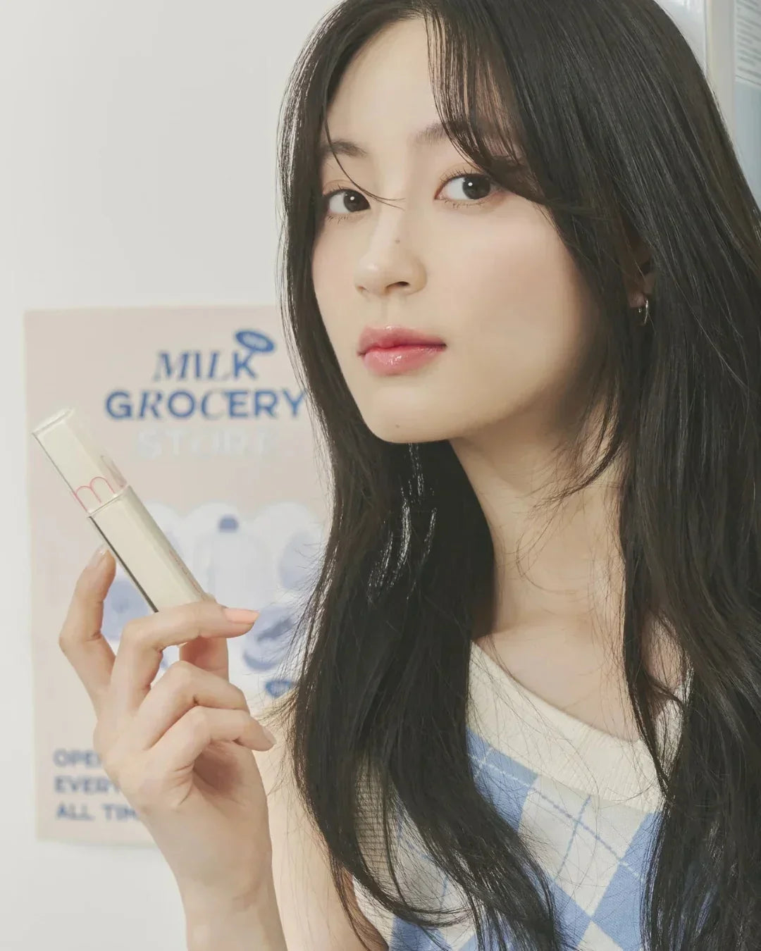 Young woman with long dark hair holding a clear cosmetic product tube with pink text indoors