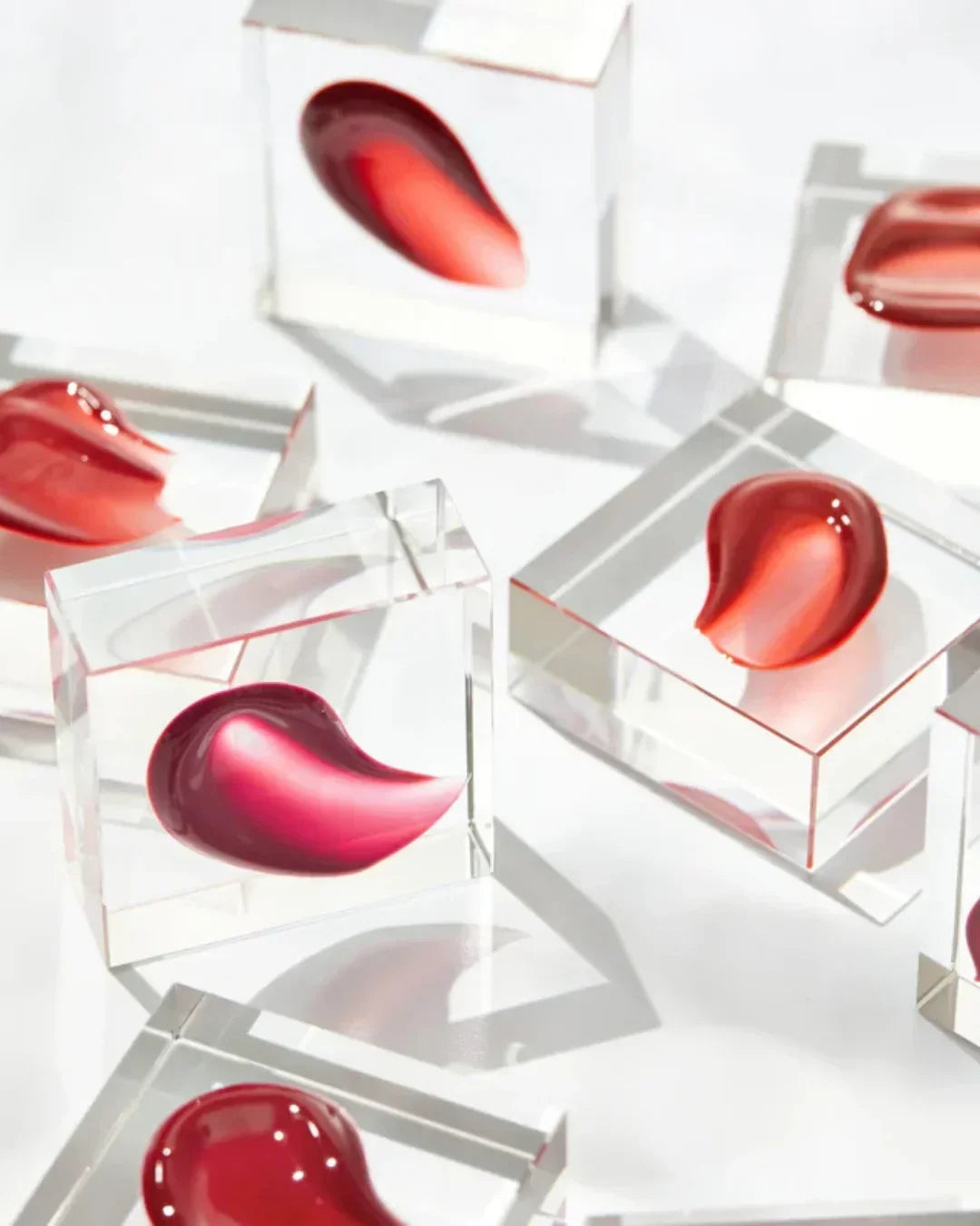 Glossy dewy water tint swatches in various red and pink shades on clear acrylic blocks