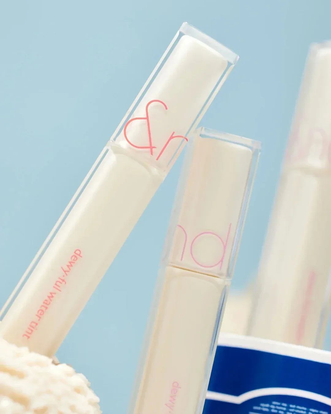 Dewyful Water Tint lip gloss tubes with clear caps on blue background