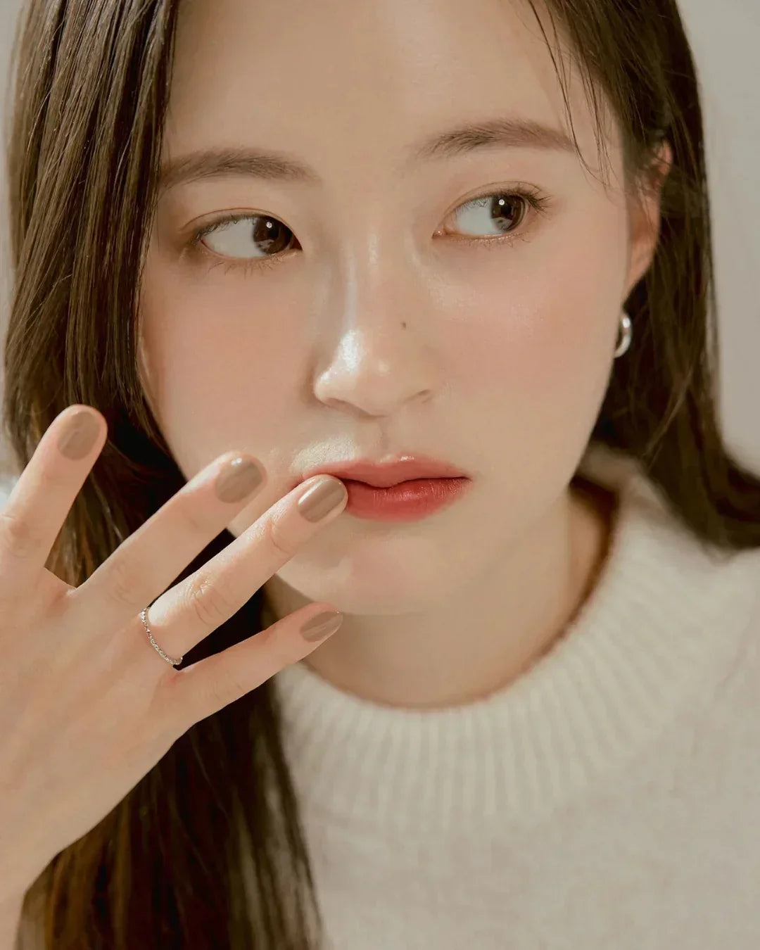Close-up of a woman with dewy skin, subtle makeup, wearing a cream sweater and silver ring