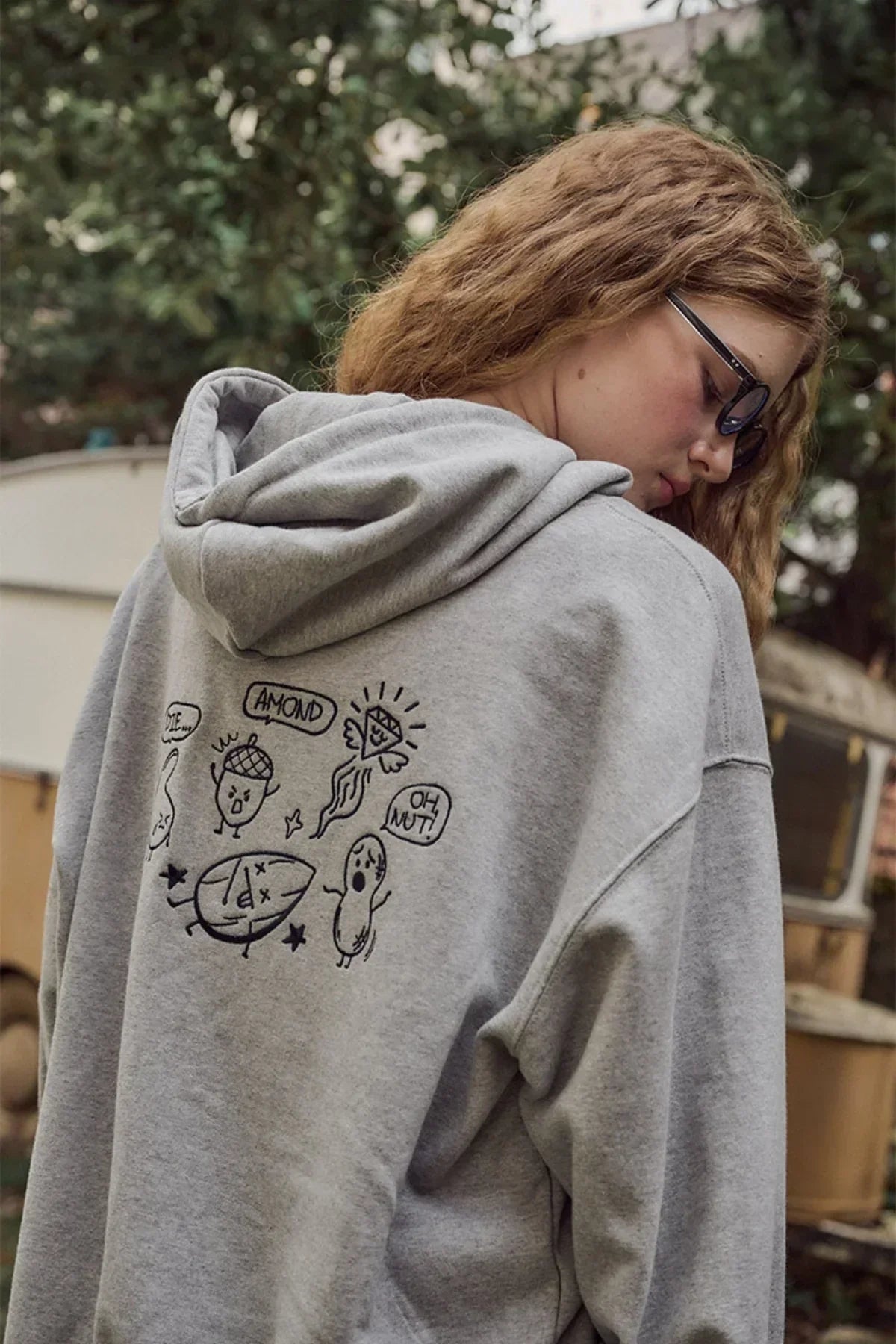 Young woman wearing gray hoodie with black cartoon nut illustrations and text outdoors