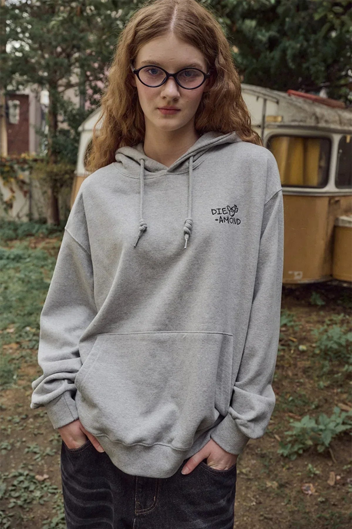 Young woman wearing gray hoodie with diamond embroidery in outdoor garden setting