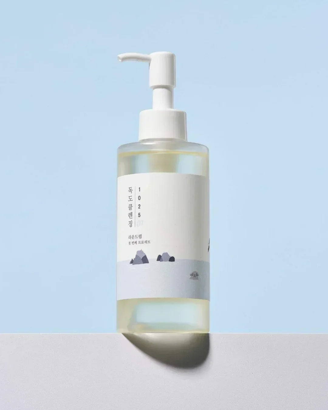 Clear plastic pump bottle of Dokdo Cleansing Oil with minimal Korean label on blue background