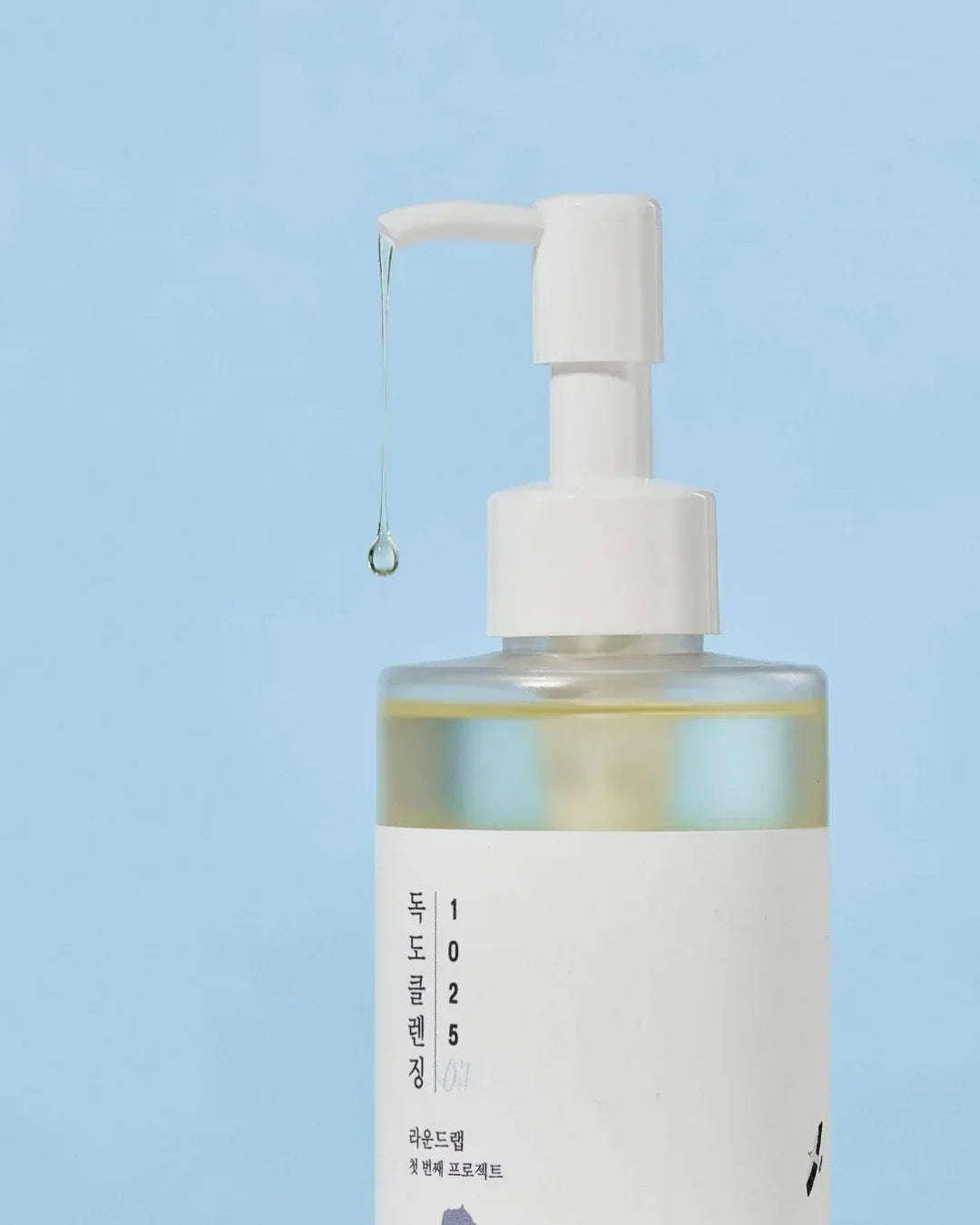 Clear Dokdo Cleansing Oil in pump bottle dispensing oil droplet on blue background