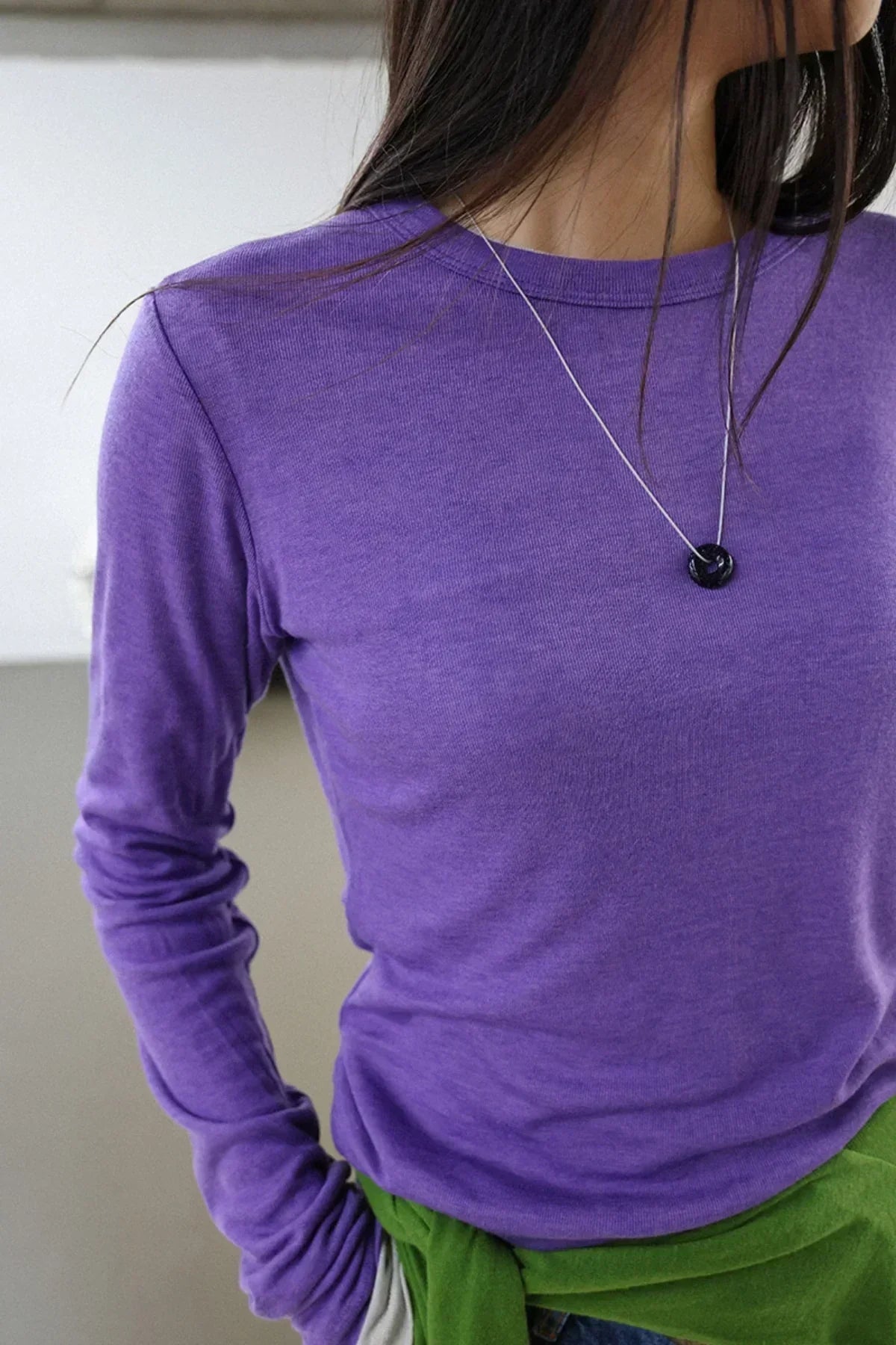 Close-up of woman wearing a purple long-sleeve shirt with a silver chain black donut-shaped pendant necklace