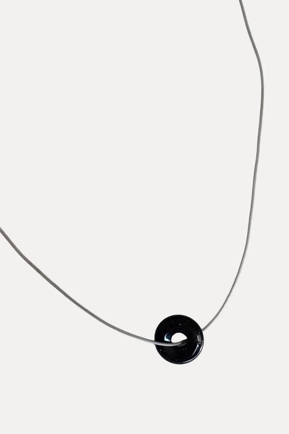 Black donut-shaped pendant on thin silver necklace chain on white background