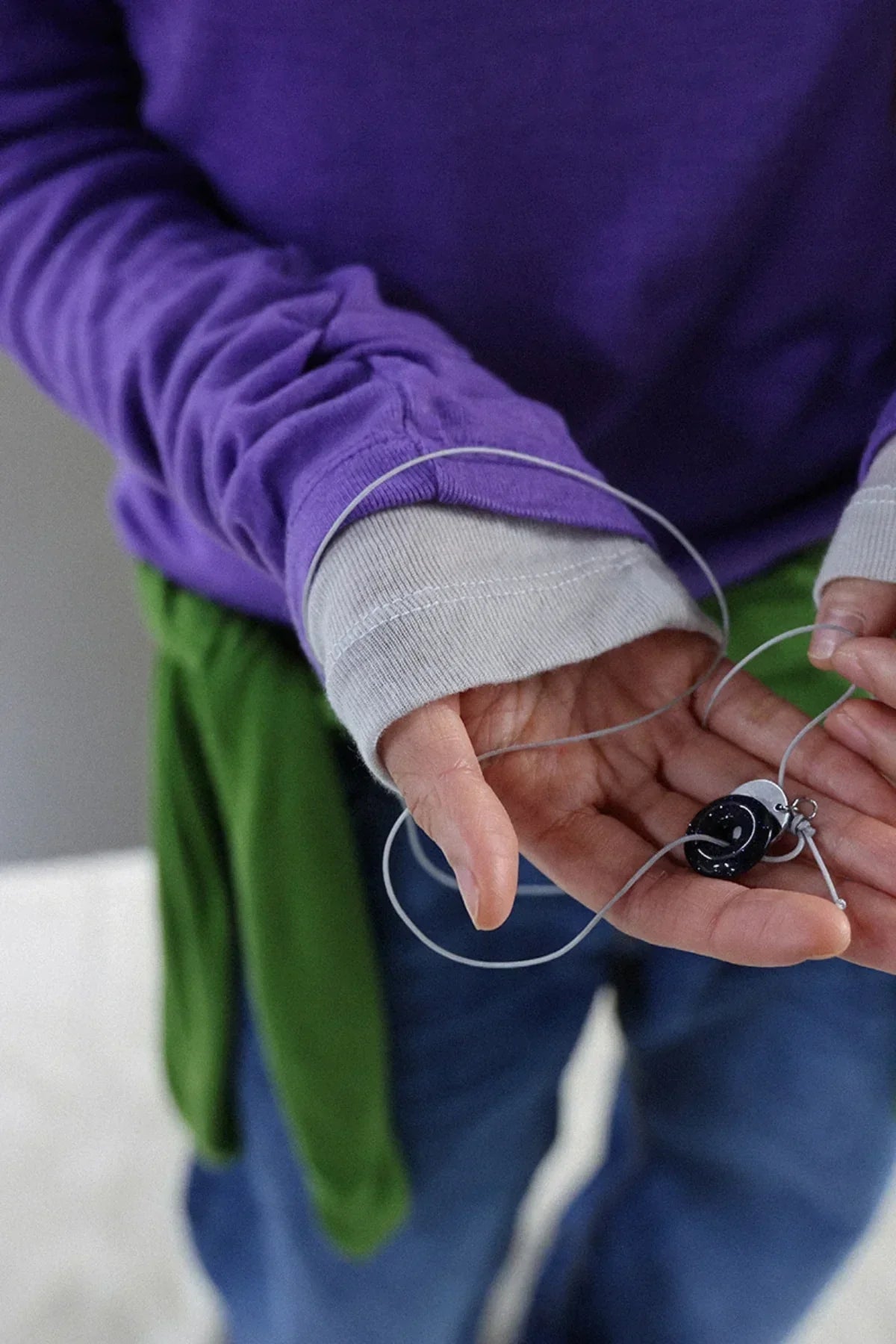 Close-up of a person in layered purple and beige sleeves holding a black donut-shaped pearl necklace with a thin cord