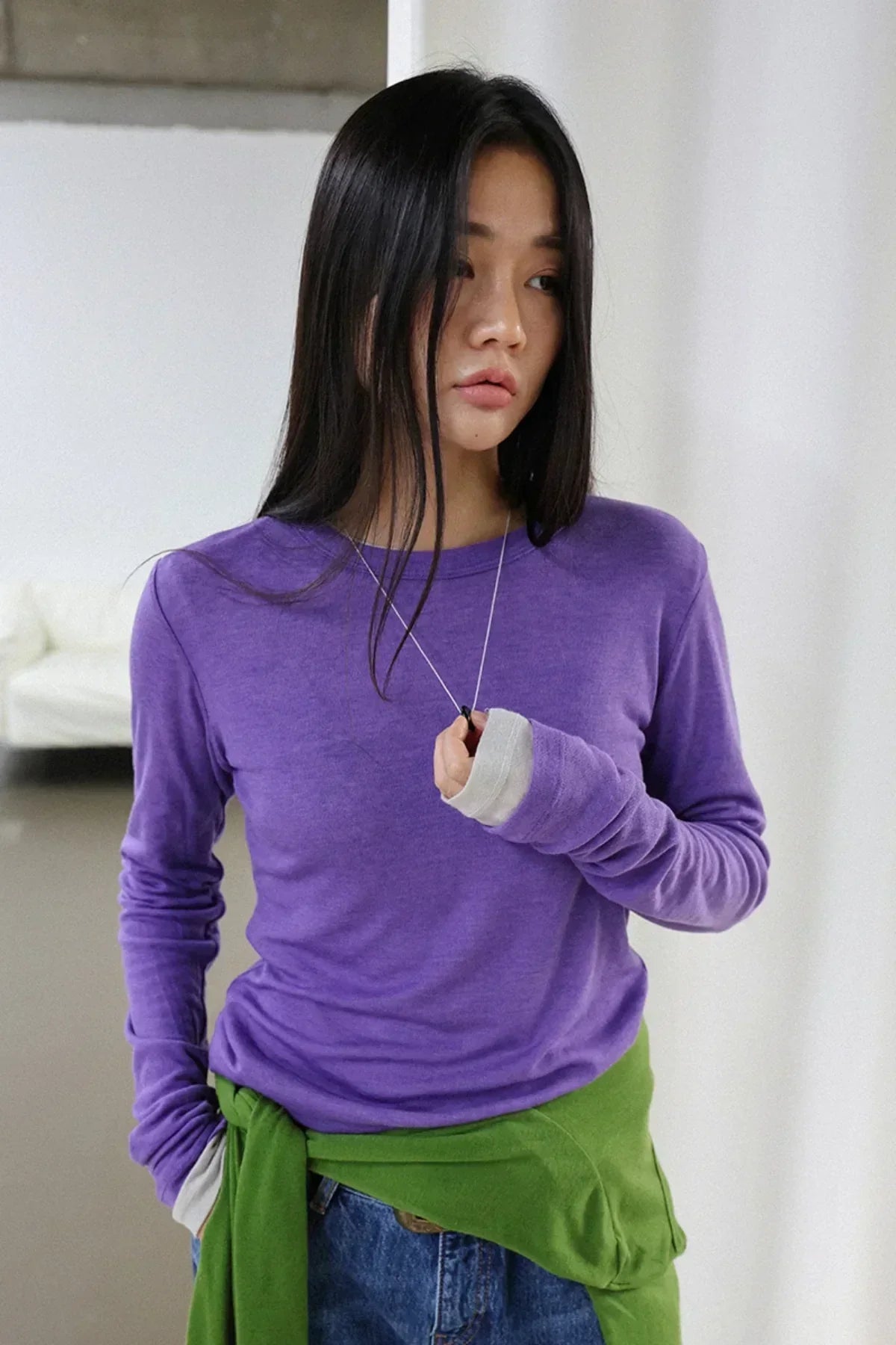 Model wearing a donut pearl necklace with a purple long-sleeve shirt and green sweater tied at waist