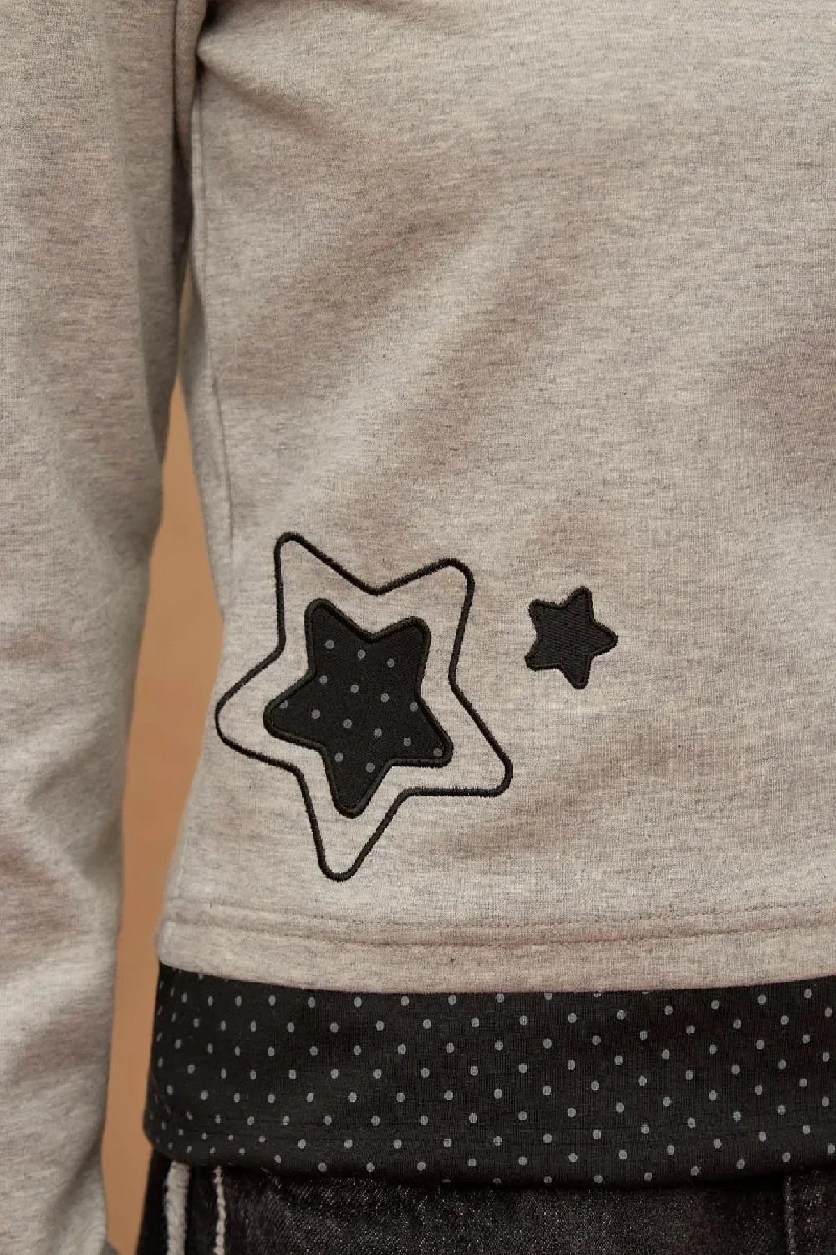 Close-up of grey long sleeve t-shirt with dot applique star design near hem and polka dot fabric detail