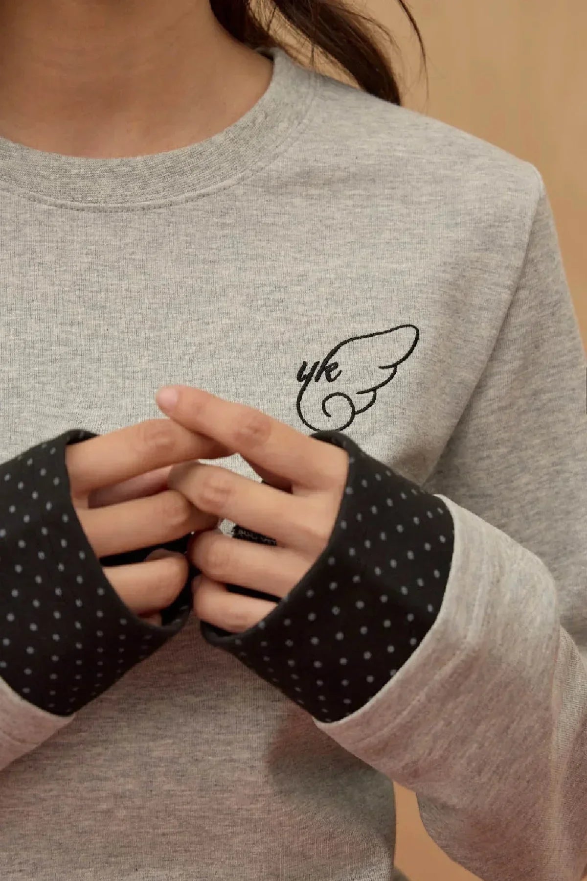 Close-up of grey layered long sleeve T-shirt with black dotted cuffs and wing logo on chest