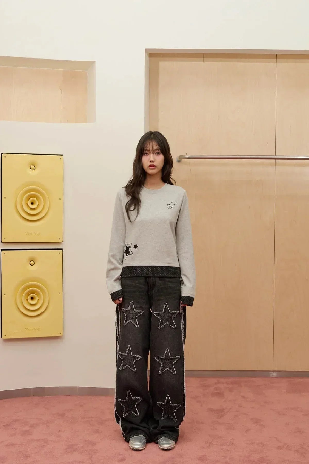 Young woman wearing grey long sleeve shirt and black wide pants with star appliques in minimal room