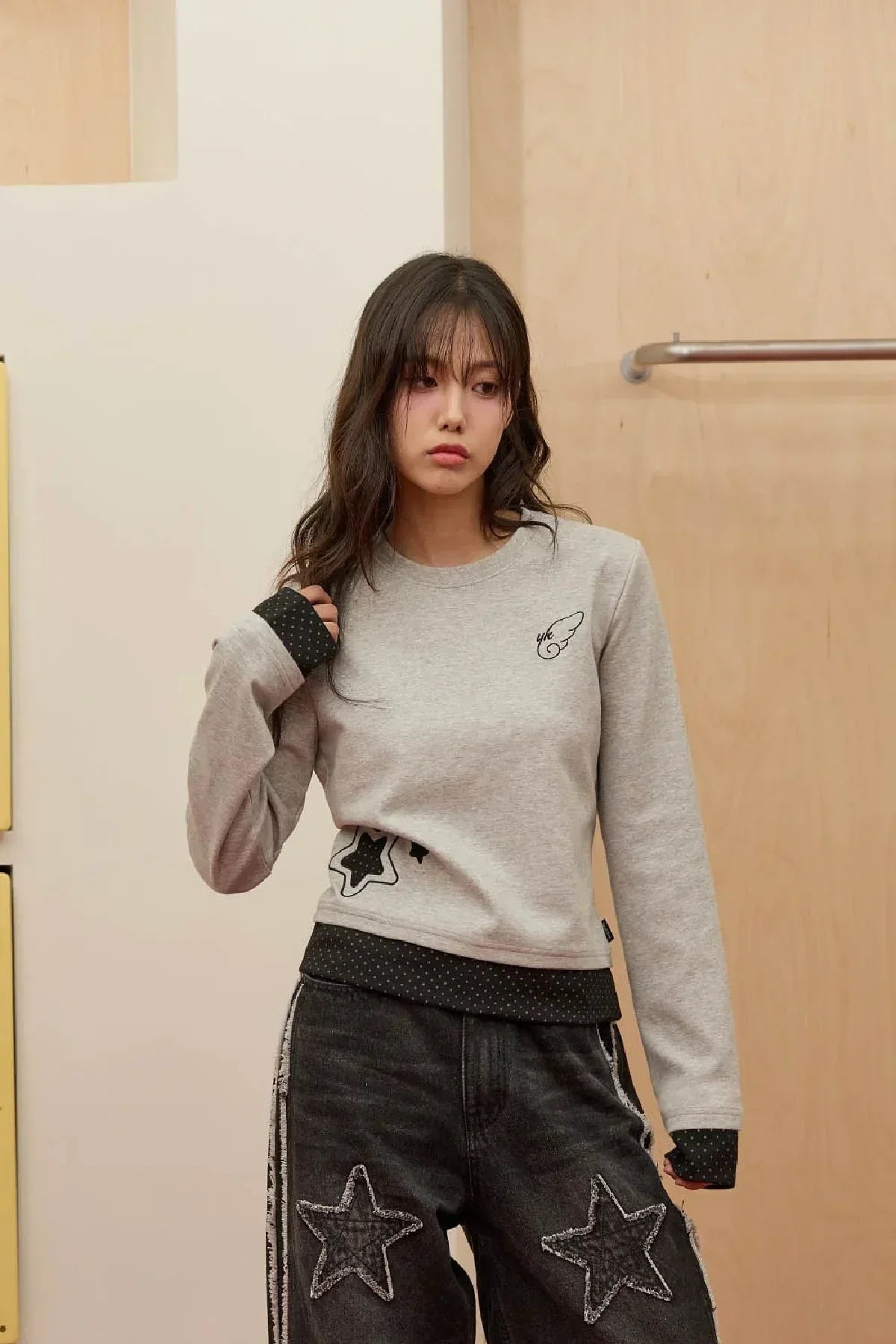 Young woman wearing grey long sleeve t-shirt with black star appliques and distressed black jeans with star patches