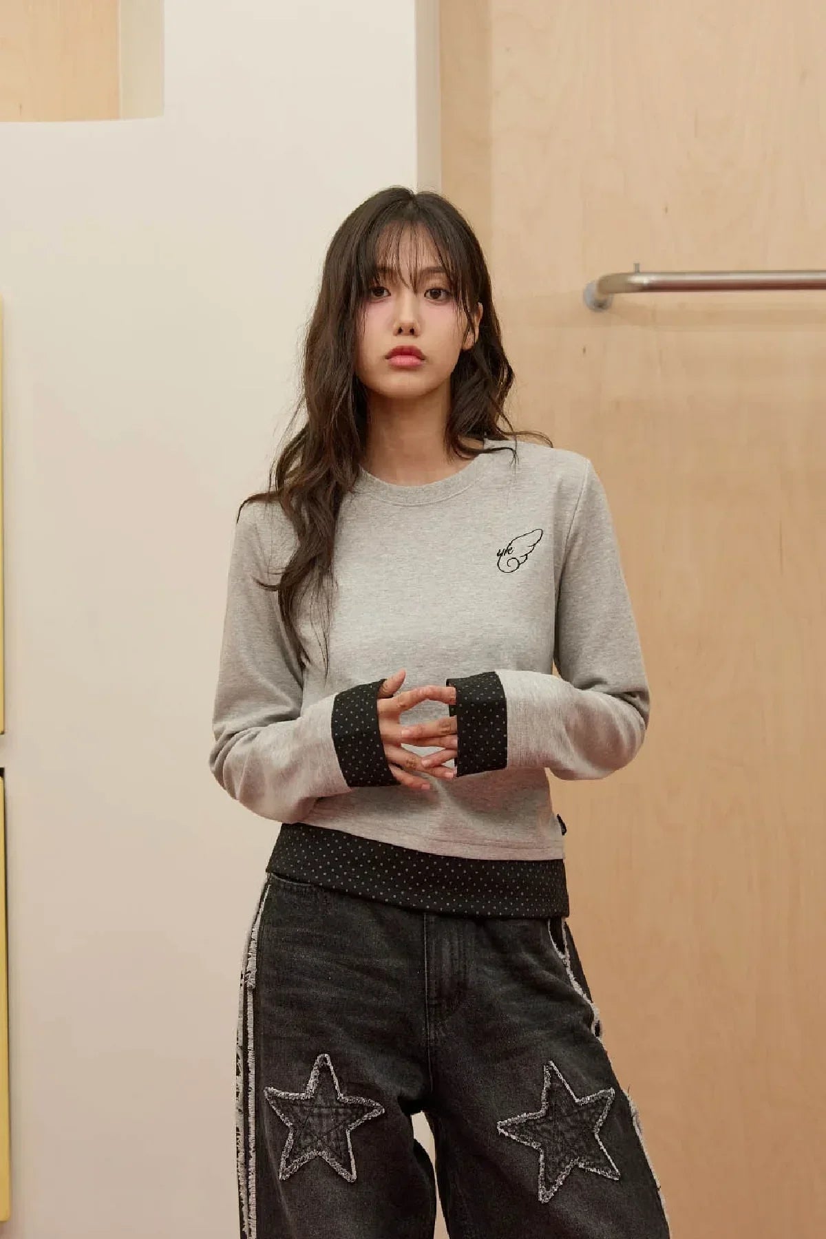 Young woman wearing grey layered long sleeve t-shirt with black star-patch jeans in minimal indoor setting