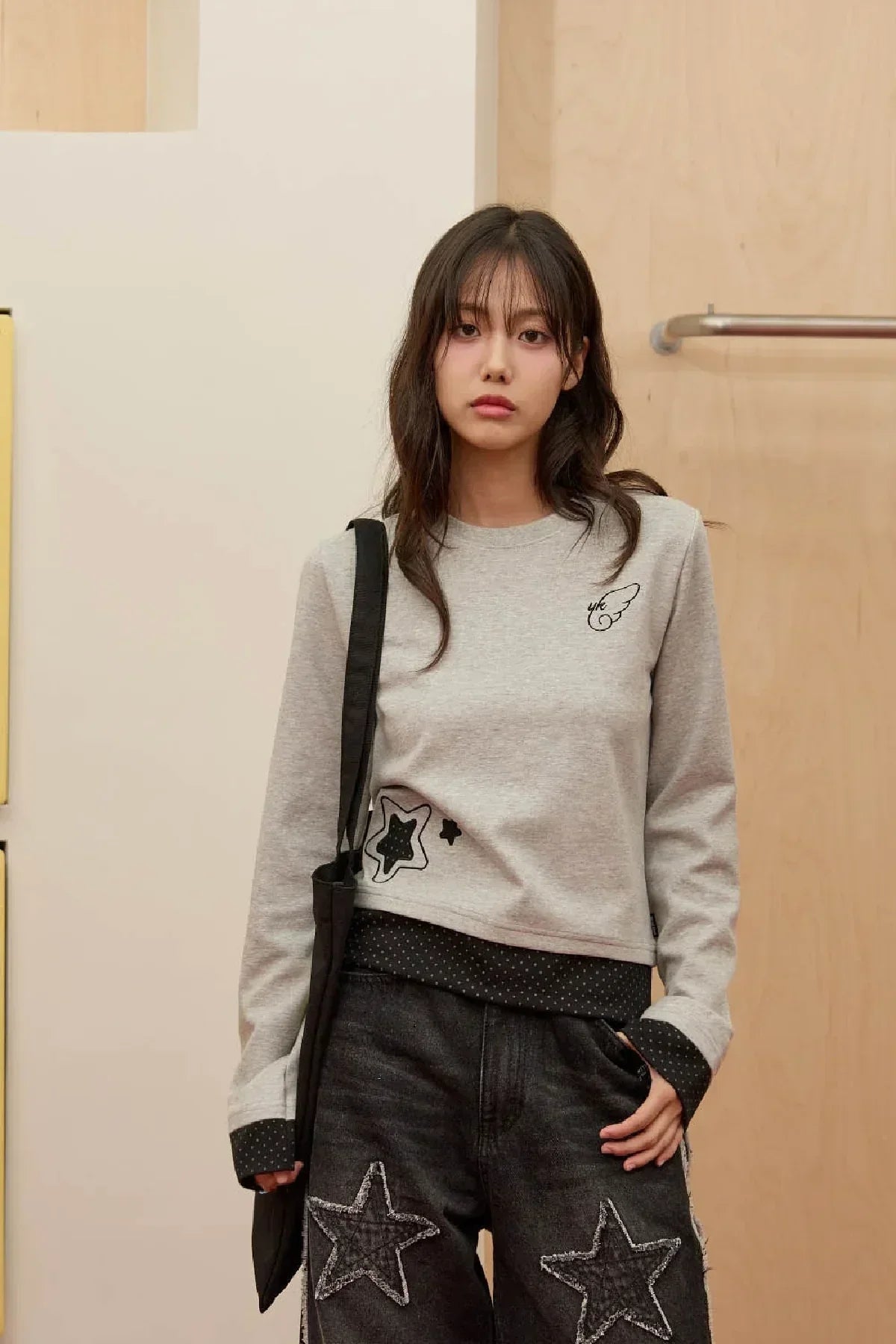 Young woman wearing grey long-sleeve t-shirt with star applique and black bag in indoor setting