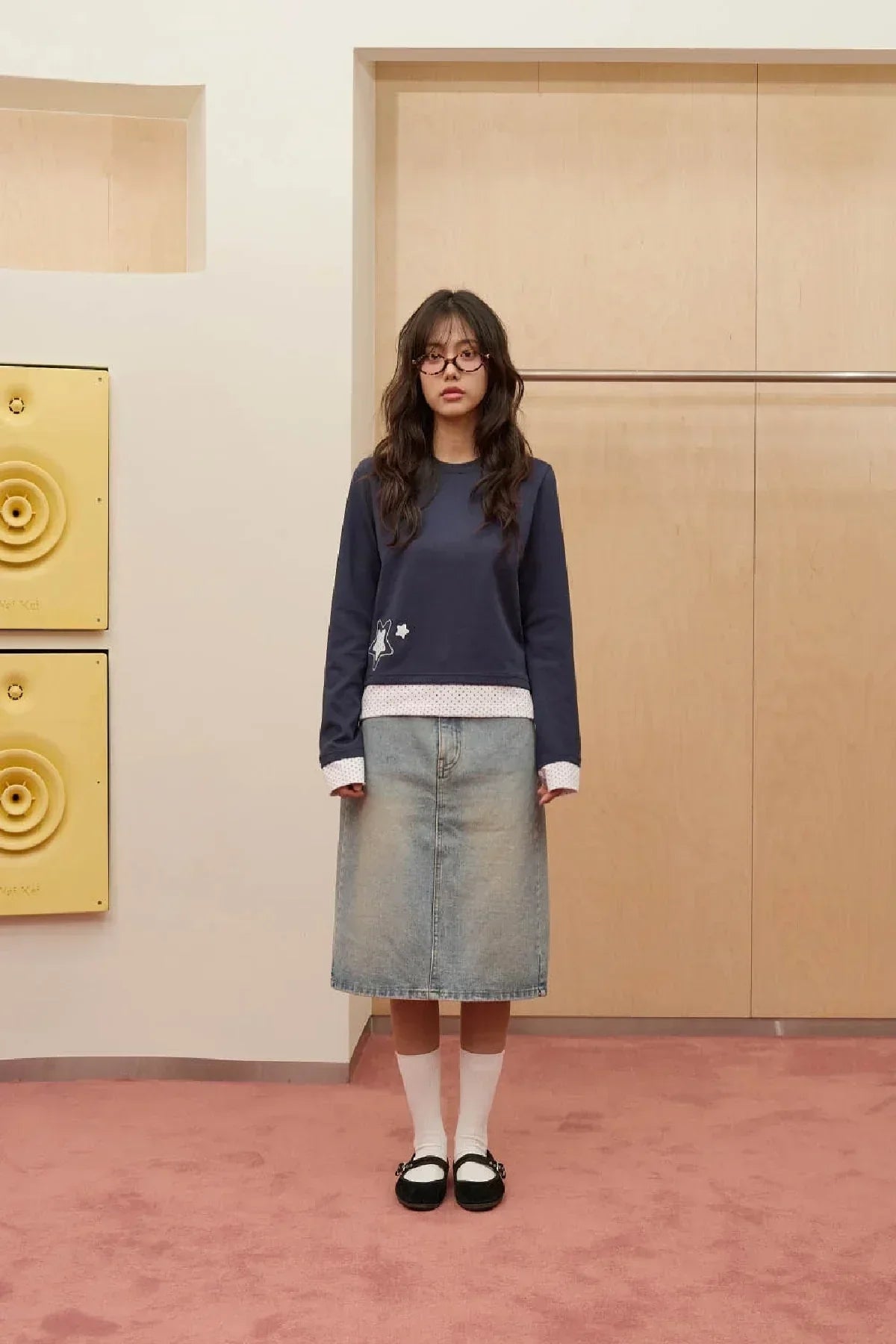 Woman wearing navy long sleeve dot applique shirt layered over white polka dot top with denim skirt indoors