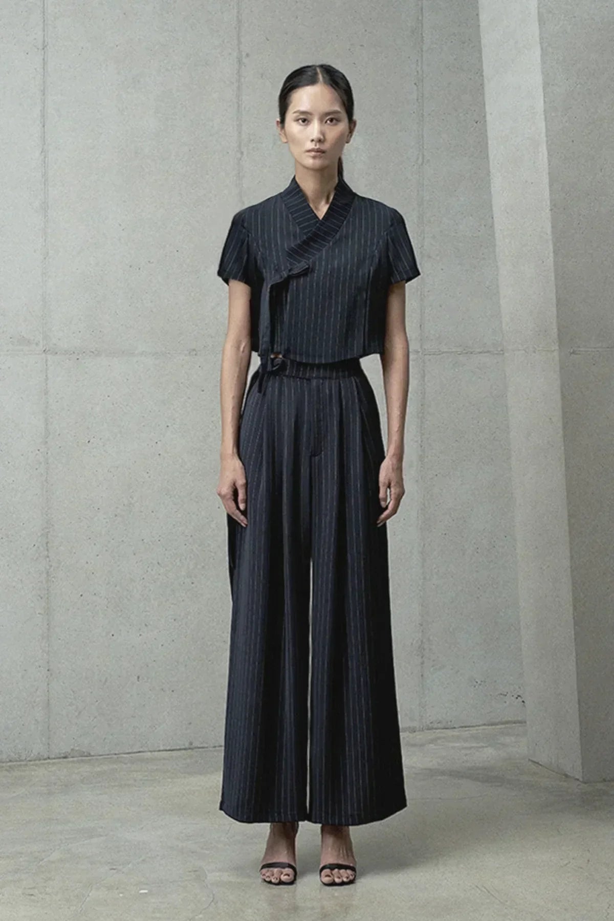 Model wearing black pinstriped short-sleeve jeogori top and wide-leg pants in minimalistic setting