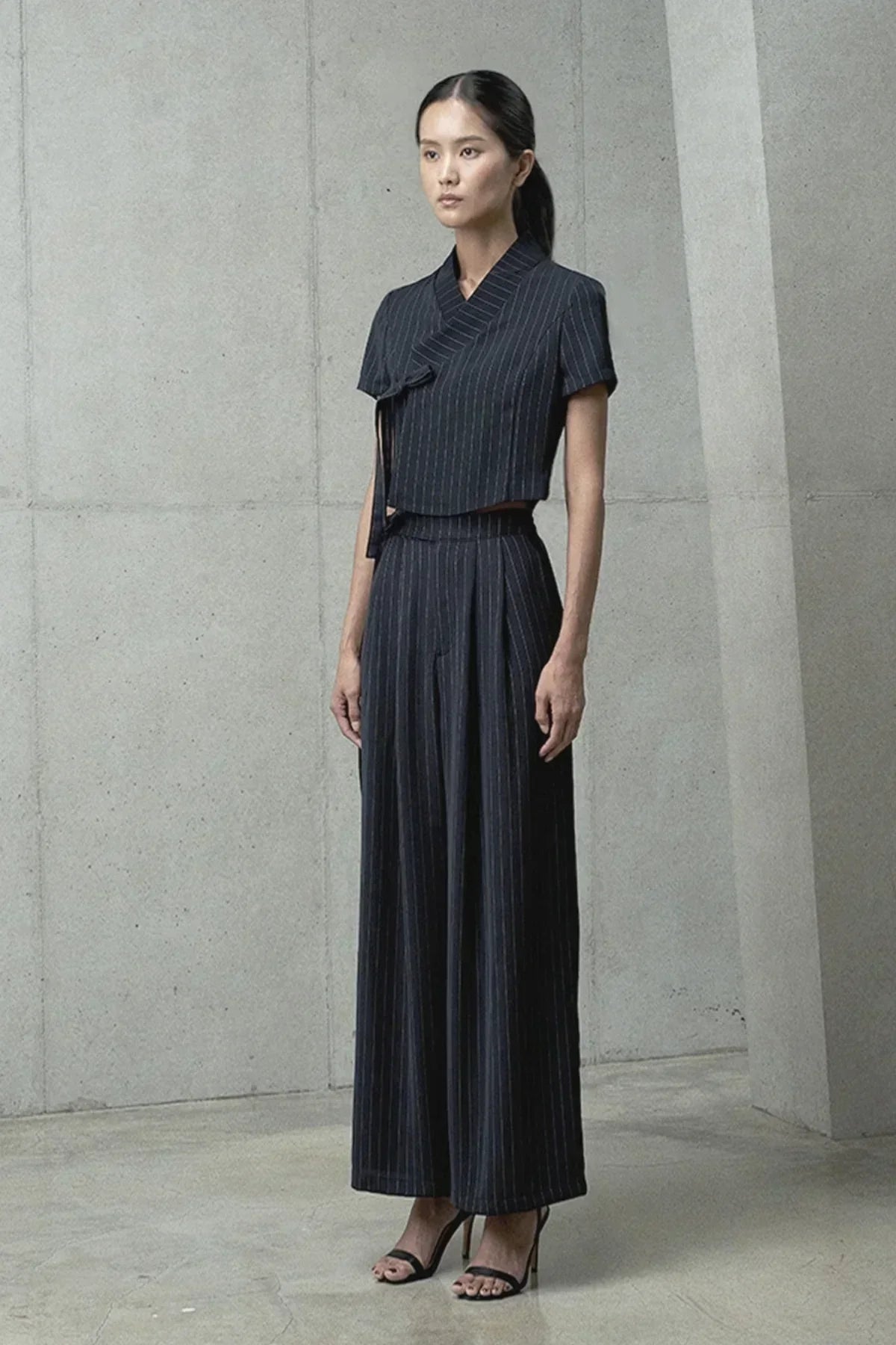 Model wearing black pinstripe short-sleeve jeogori top and wide-leg pants in modern minimalist setting