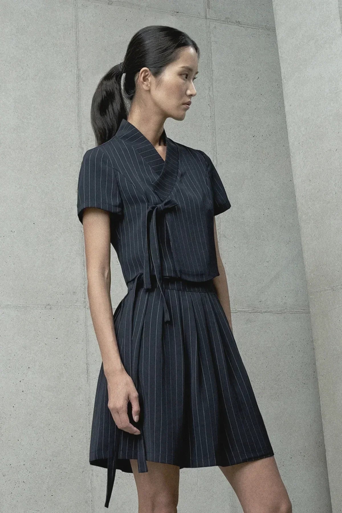 Woman in black pinstripe hanbok-style short dress posing against concrete wall