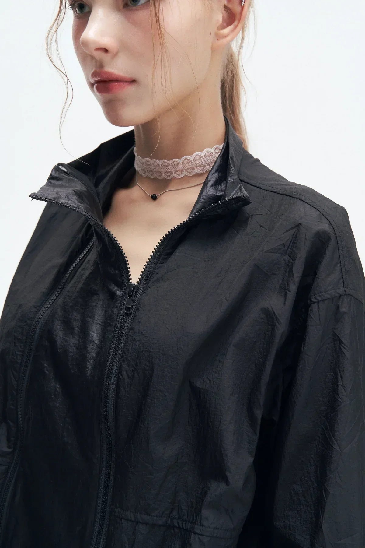 Close-up of woman wearing black windbreaker jacket with double zipper and lace choker on white background