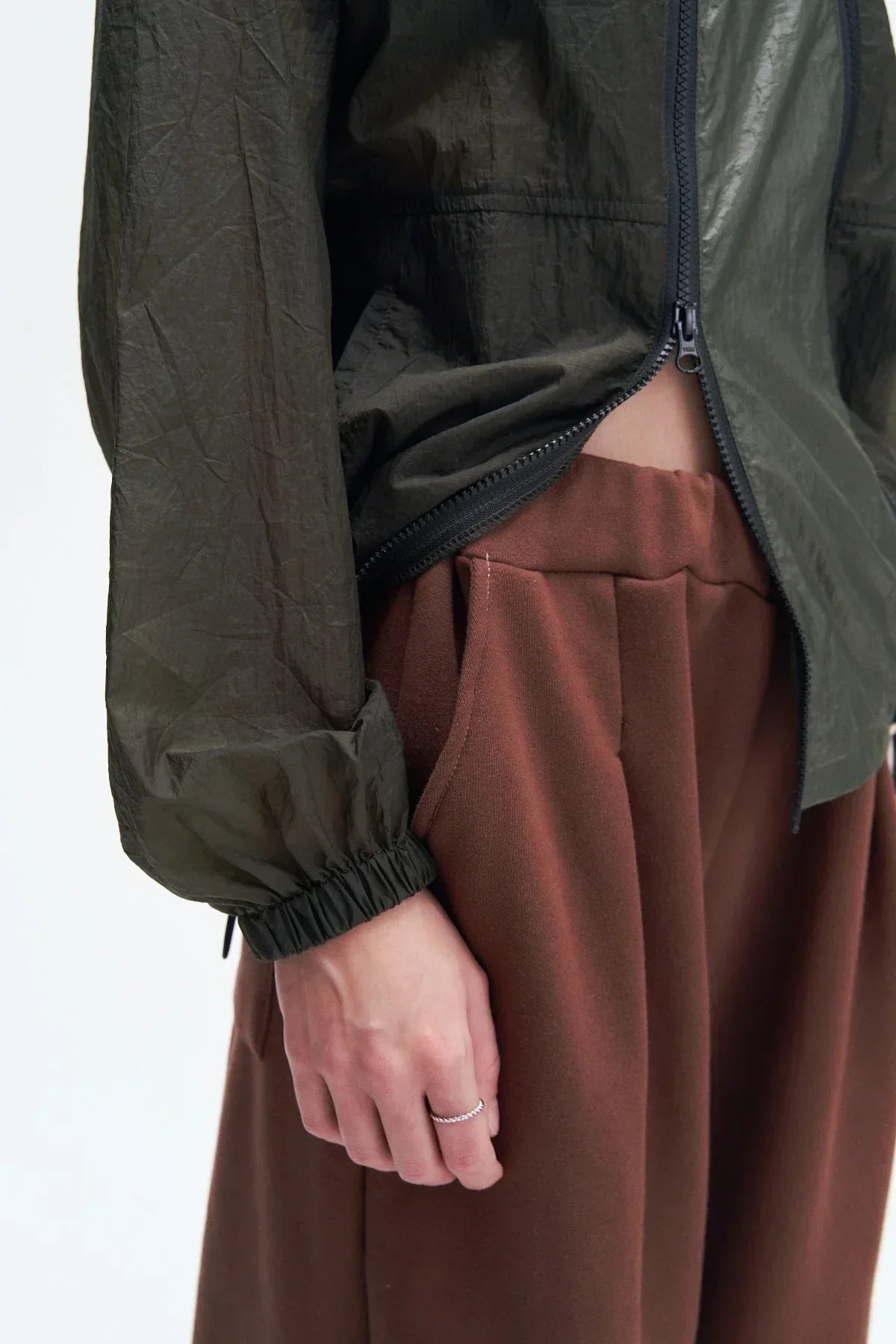 Close-up of a person wearing a black double zipper jacket with elastic cuffs and brown pleated pants