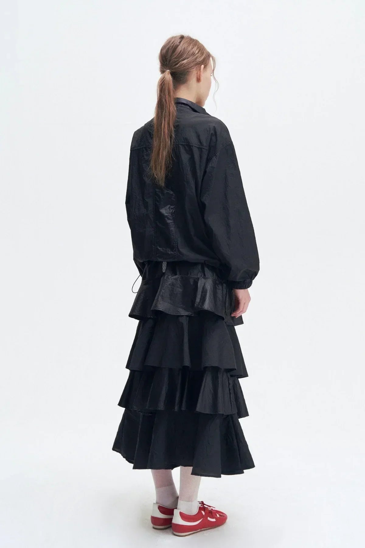 Model wearing a black double-zipper jacket and tiered black skirt with red and white sneakers