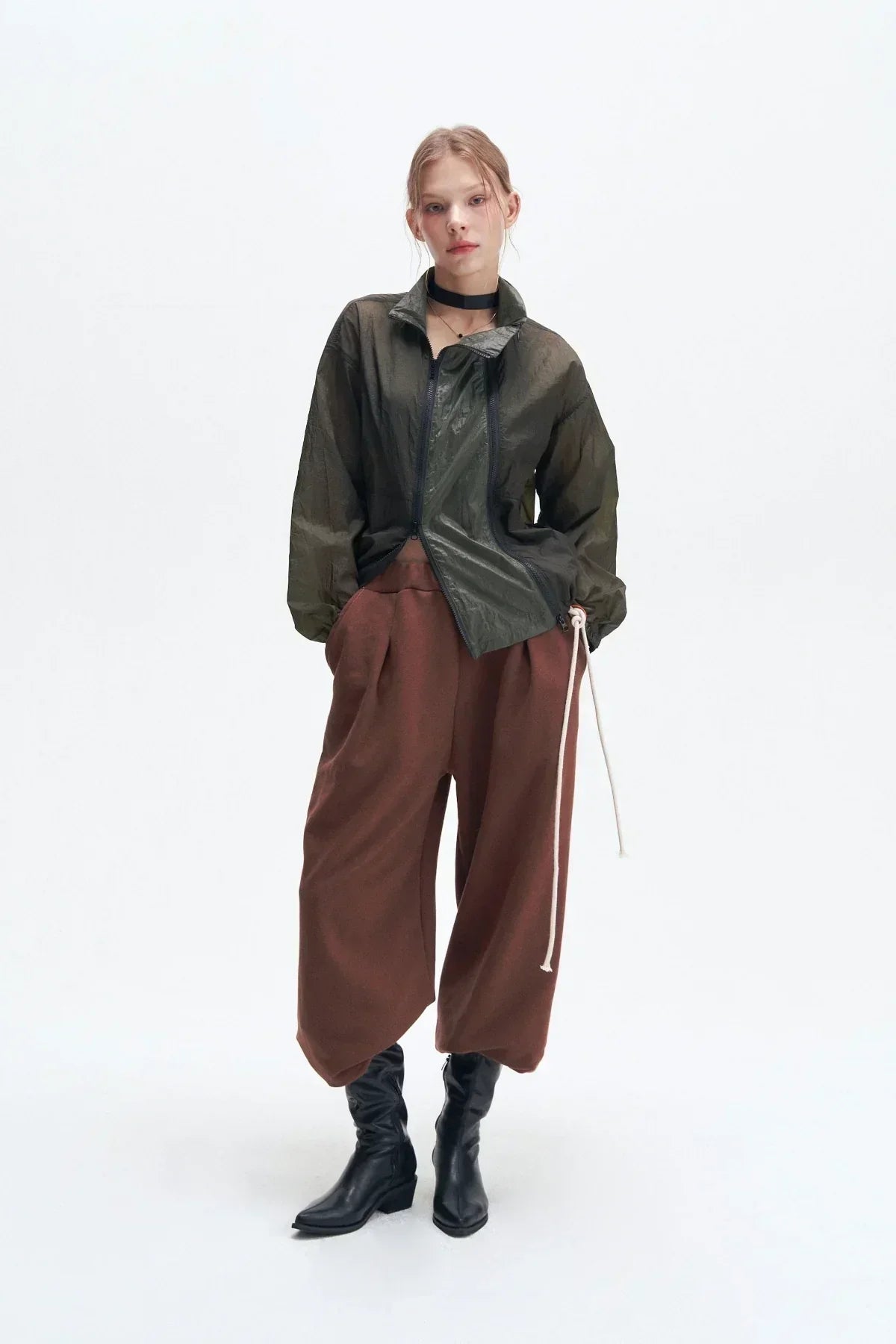 Model wearing khaki double zipper windbreaker jacket, loose brown pants, black boots, and black choker