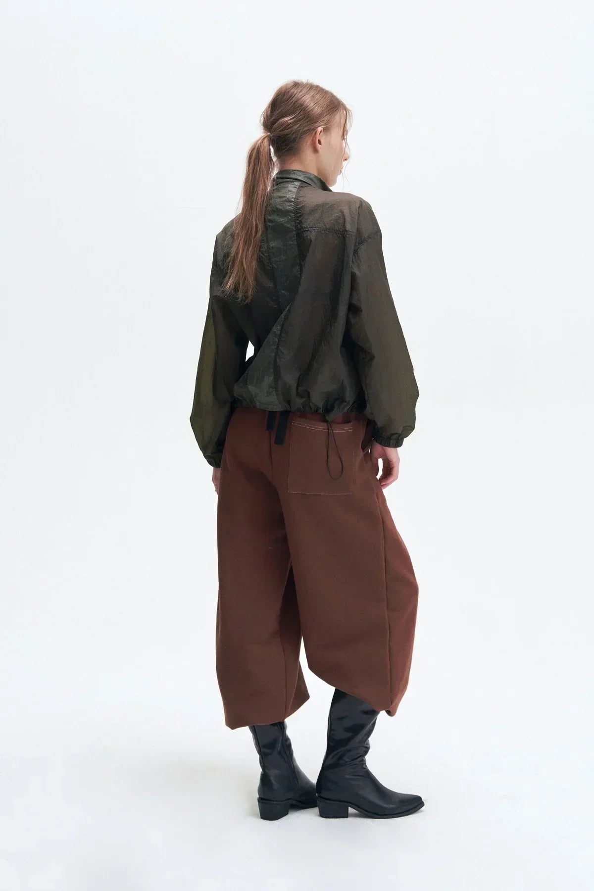Model wearing dark olive lightweight jacket, brown wide pants, and black boots on white background