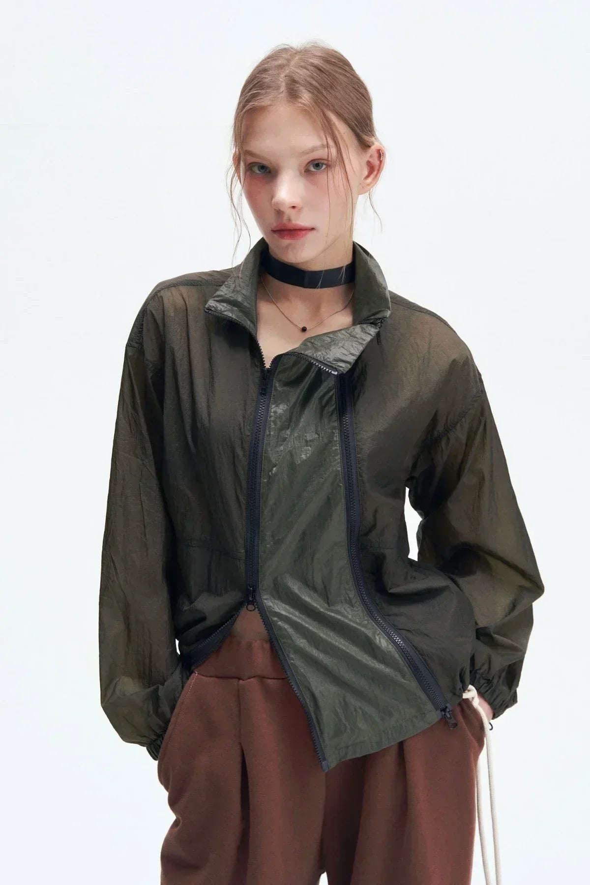 Young woman wearing a khaki double zipper windbreaker jacket and brown pants against white background