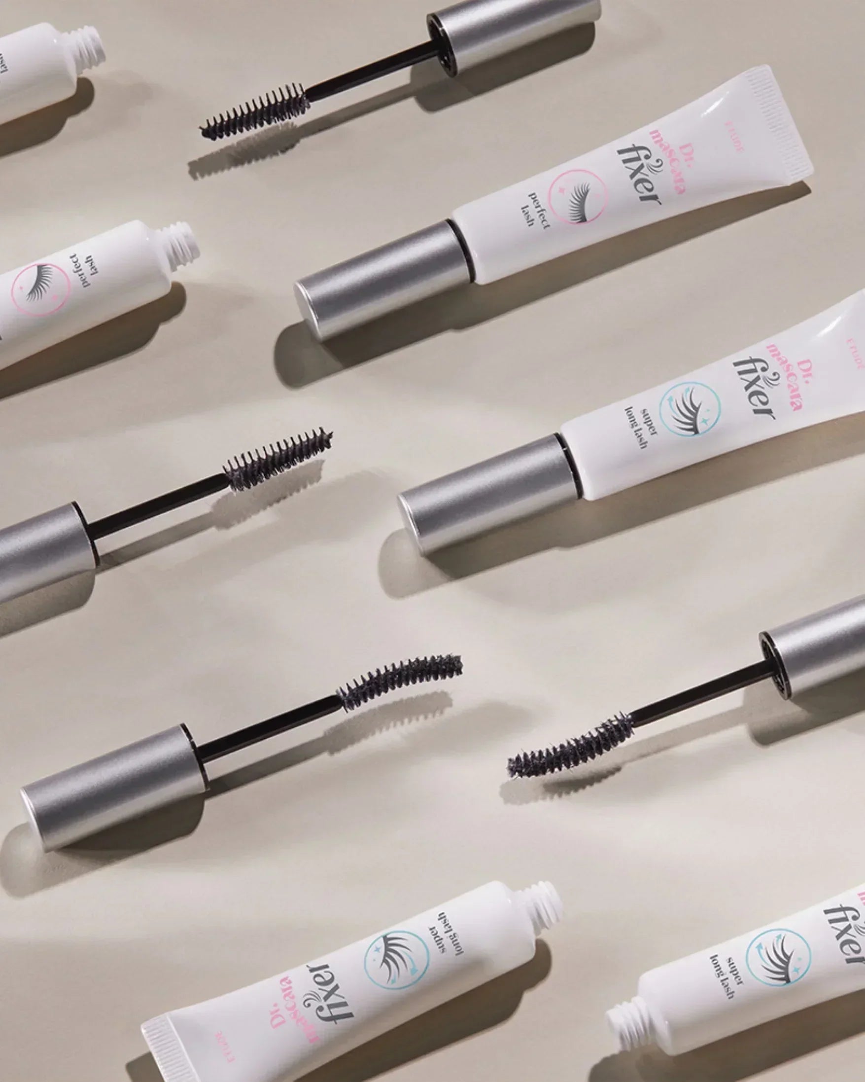 Multiple tubes and wands of Dr. Mascara Fixer eyelash mascara laid on a beige surface