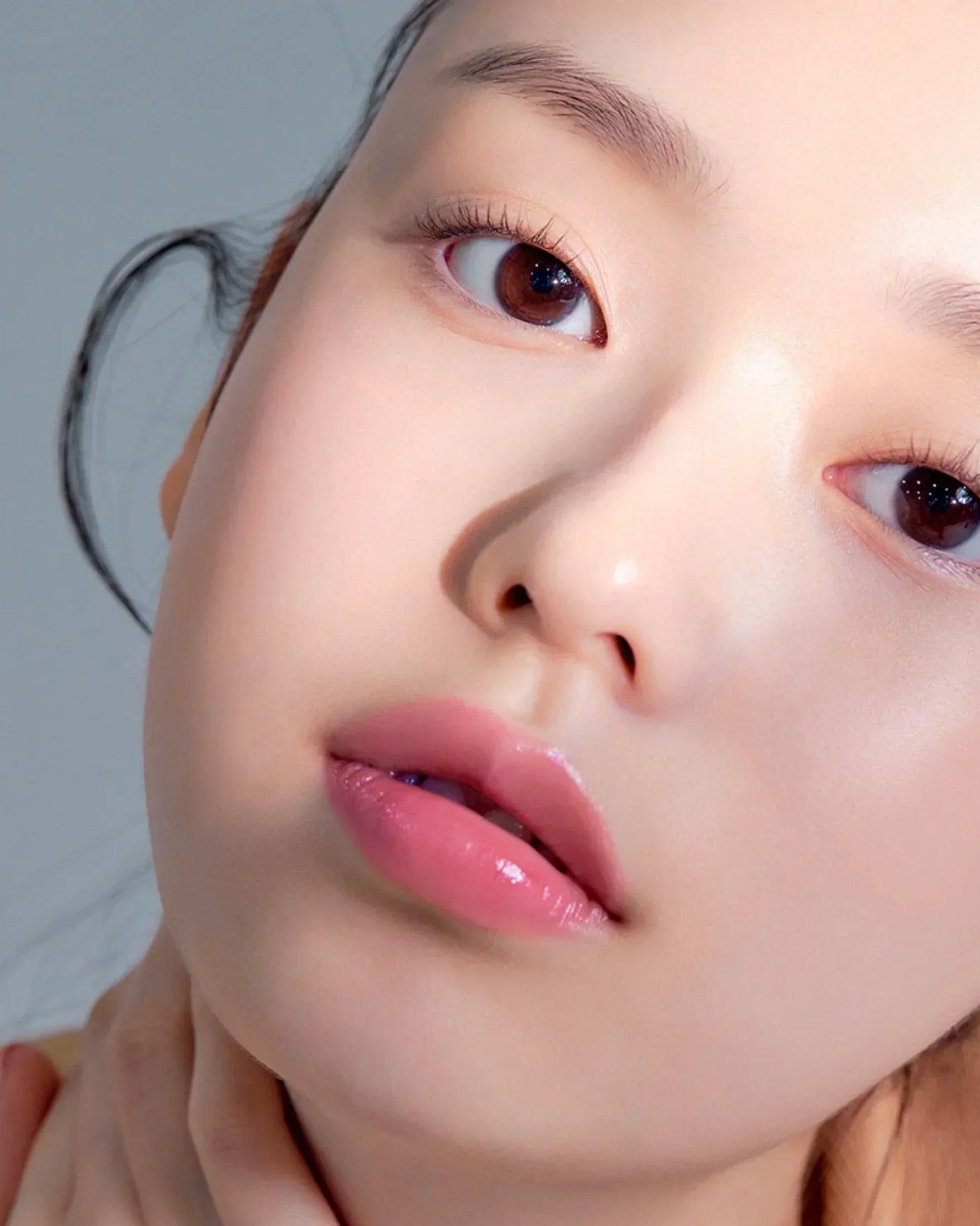 Close-up of a young woman with natural makeup, glossy pink lips, and long curled eyelashes