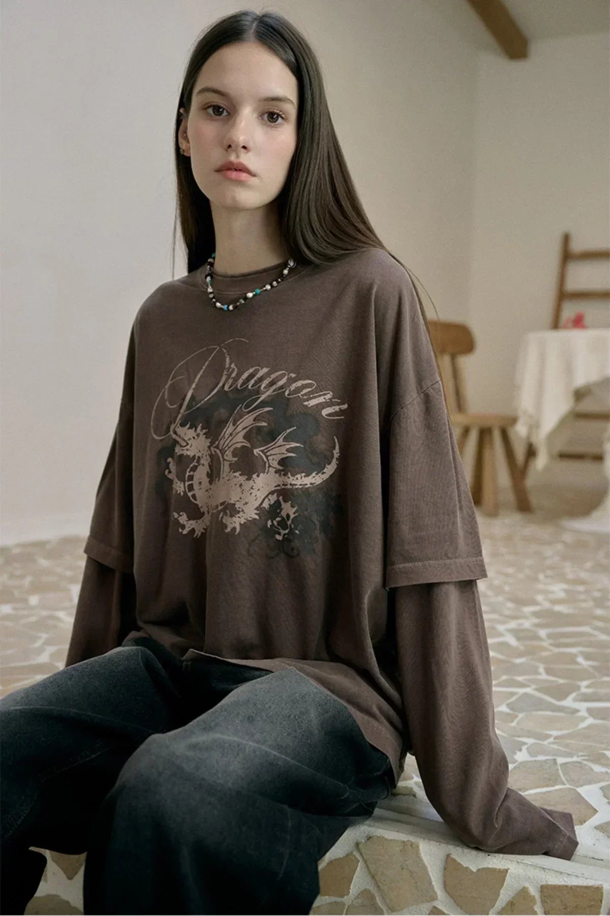 Young woman in brown layered long sleeve shirt with dragon print sitting on mosaic floor indoors