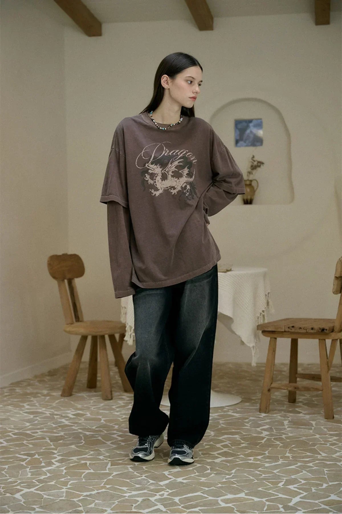 Woman wearing brown Dragon layered pigment long sleeve top with loose black pants and sneakers indoors