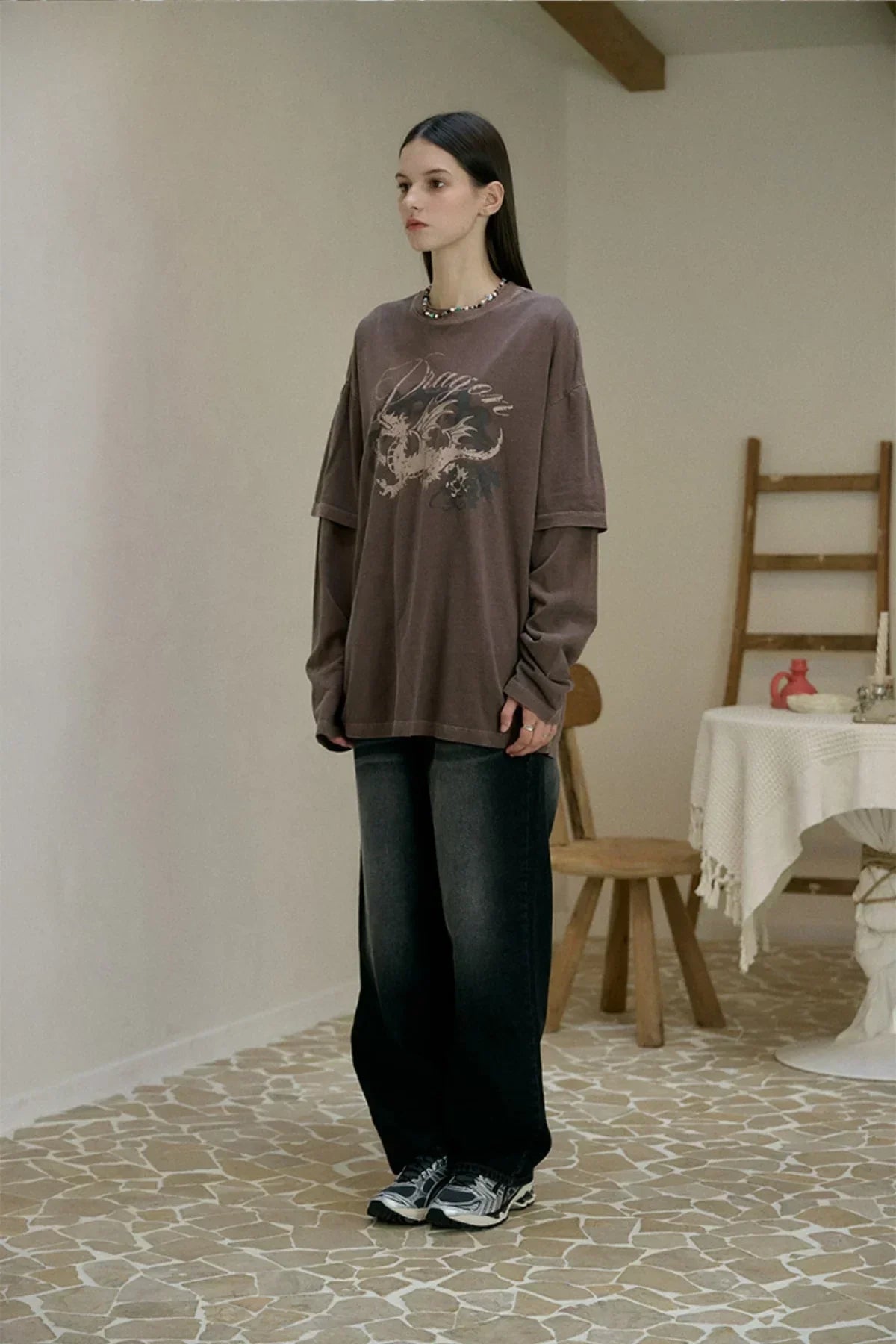 Woman wearing brown dragon graphic layered long sleeve shirt and black wide-leg pants indoors