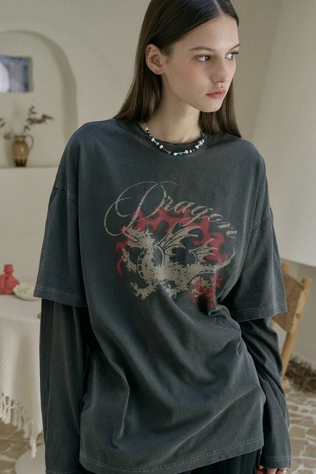 Woman wearing dark layered long-sleeve and short-sleeve tee with distressed dragon print and beaded necklace