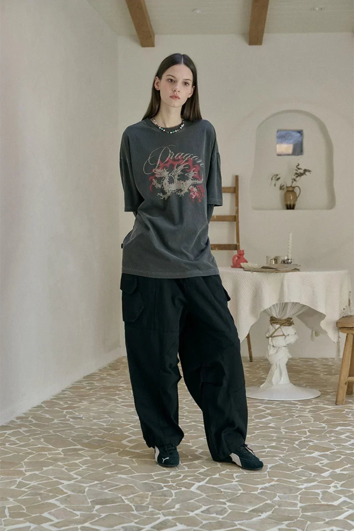 Young woman wearing smoke black dragon layered pigment long sleeve T-shirt and baggy black cargo pants in a minimal room