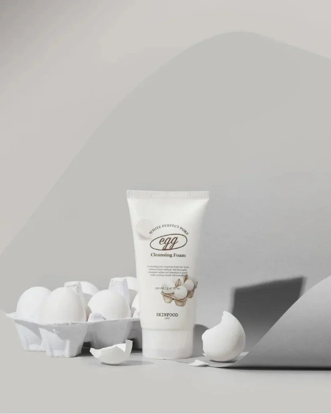 Skinfood White Perfect Pore Egg Cleansing Foam tube with egg carton and broken eggshells on gray background