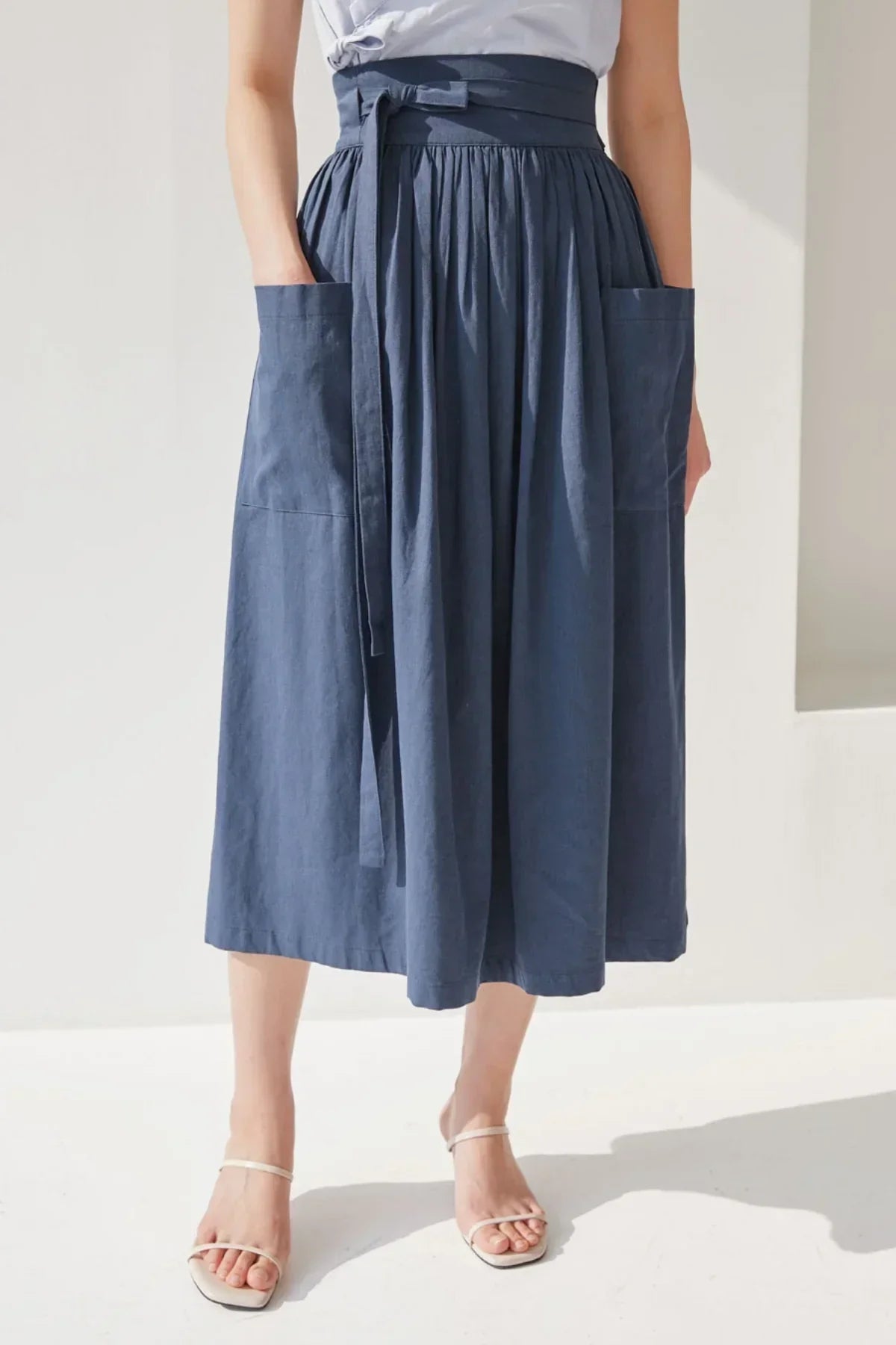 Woman wearing navy blue denim midi skirt with large front pockets and waist tie belt