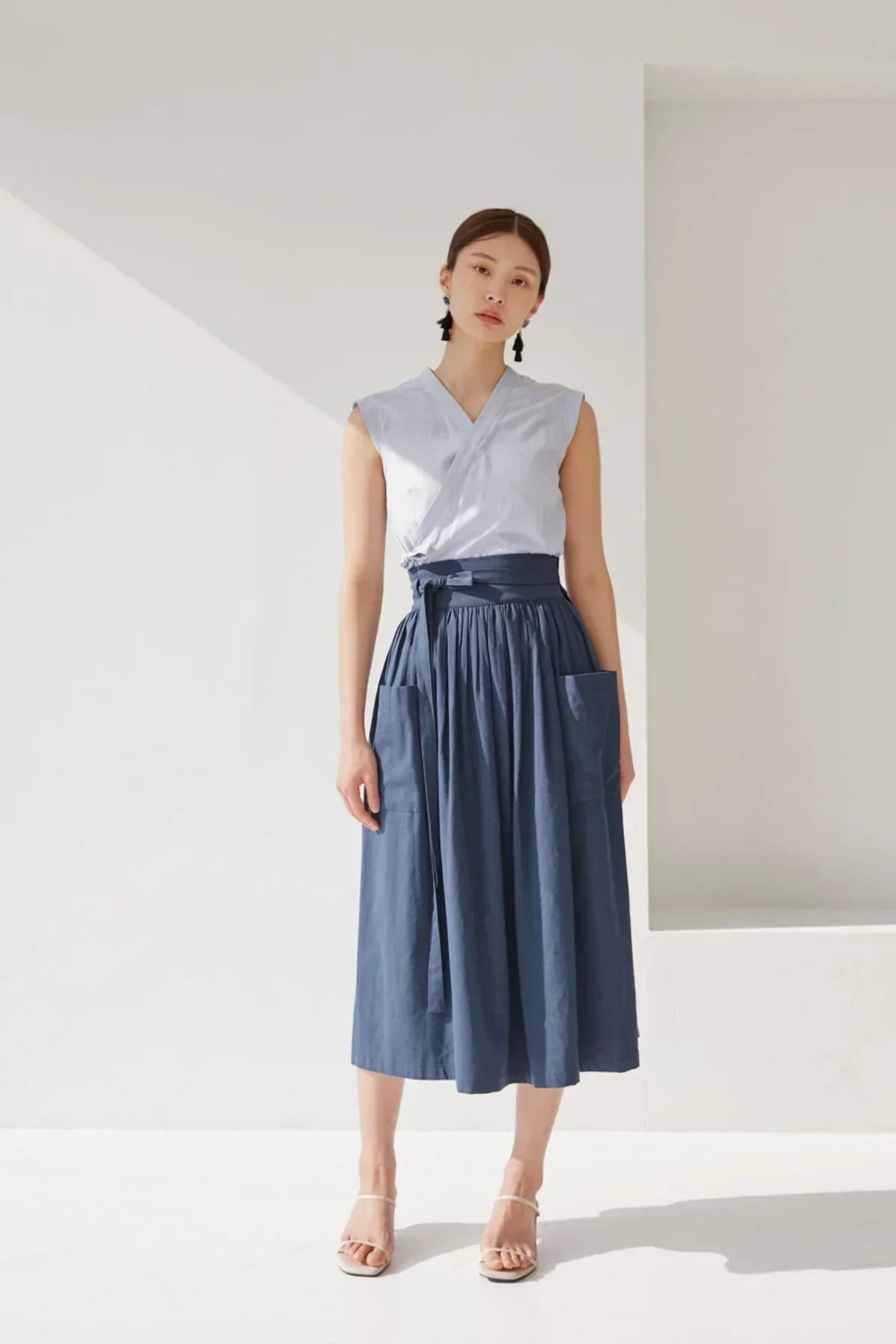 Woman wearing a navy blue high-waisted midi skirt with pockets and a sleeveless light blue wrap top